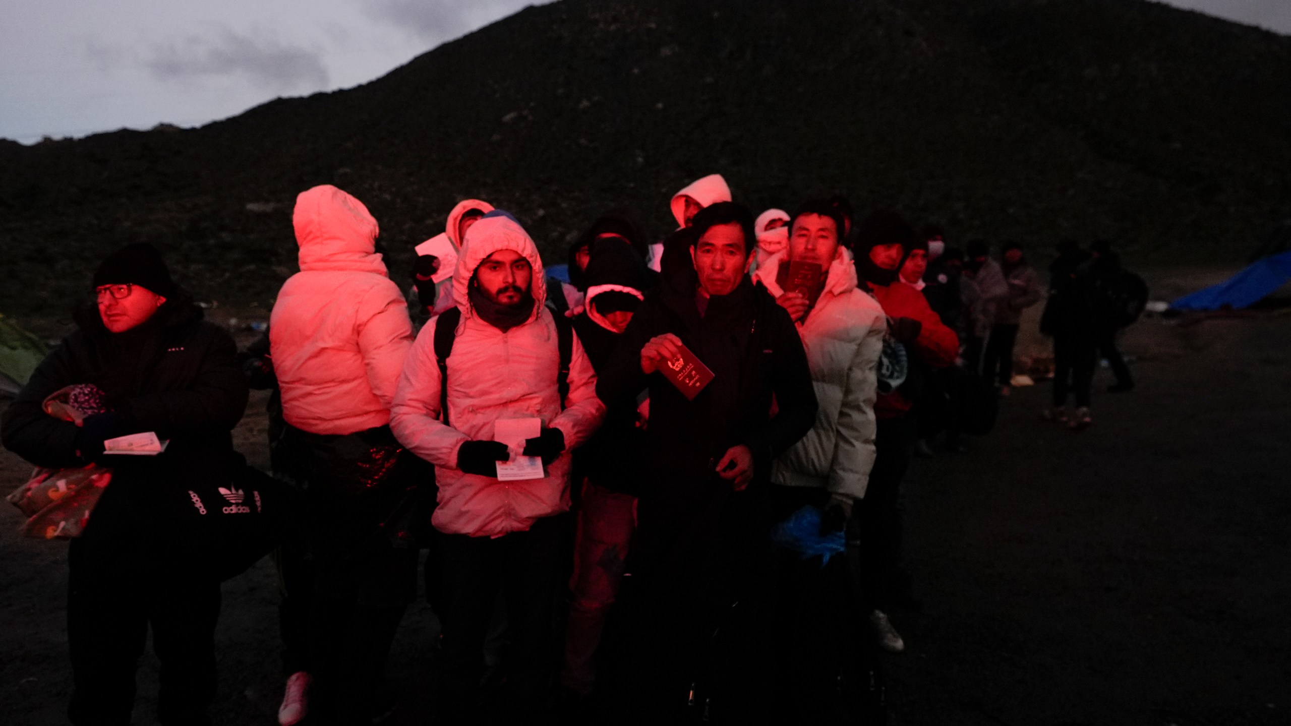 Asylum-seeking migrants hold their documents as they line up in a makeshift, mountainous campsite to be processed after crossing the border with Mexico, Friday, Feb. 2, 2024, near Jacumba Hot Springs, Calif. (AP Photo/Gregory Bull)