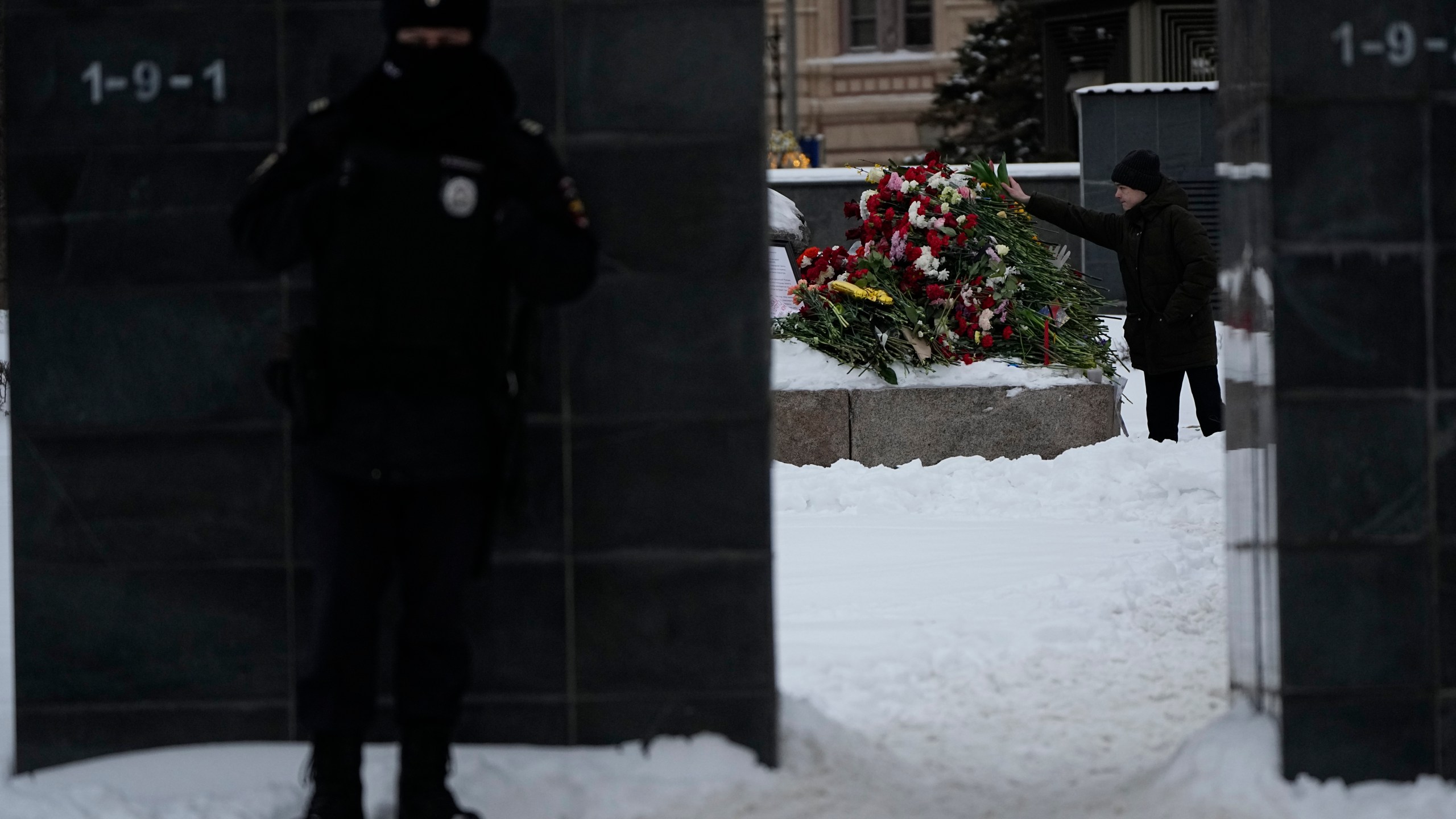 A policeman guards as a young man lay flowers paying the last respect to Alexei Navalny at the monument, a large boulder from the Solovetsky islands, where the first camp of the Gulag political prison system was established, near the historical the Federal Security Service (FSB, Soviet KGB successor) building, in Moscow, Russia, on Saturday morning, Feb. 17, 2024. Russian authorities say that Alexei Navalny, the fiercest foe of Russian President Vladimir Putin who crusaded against official corruption and staged massive anti-Kremlin protests, died in prison. He was 47. (AP Photo/Alexander Zemlianichenko)