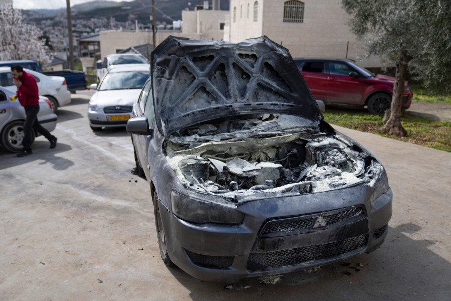 A man walks past a vehicle allegedly set ablaze by Jewish West Bank settlers in the Palestinian West Bank village of Turmus Ayya, Sunday, Feb. 18, 2024. Village residents claimed that settlers raided the outskirts of the village overnight, setting fire to a car and spaying graffiti on the walls of homes. (AP Photo/Nasser Nasser)