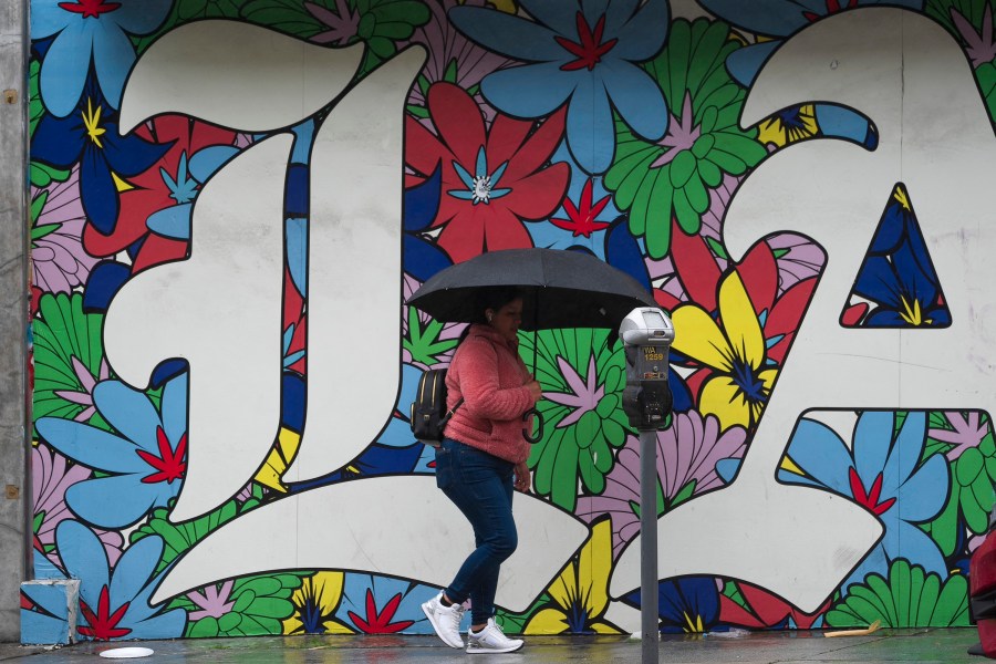 A woman walk under the rain in Los Angeles, Monday, Feb. 19, 2024. (AP Photo/Damian Dovarganes)