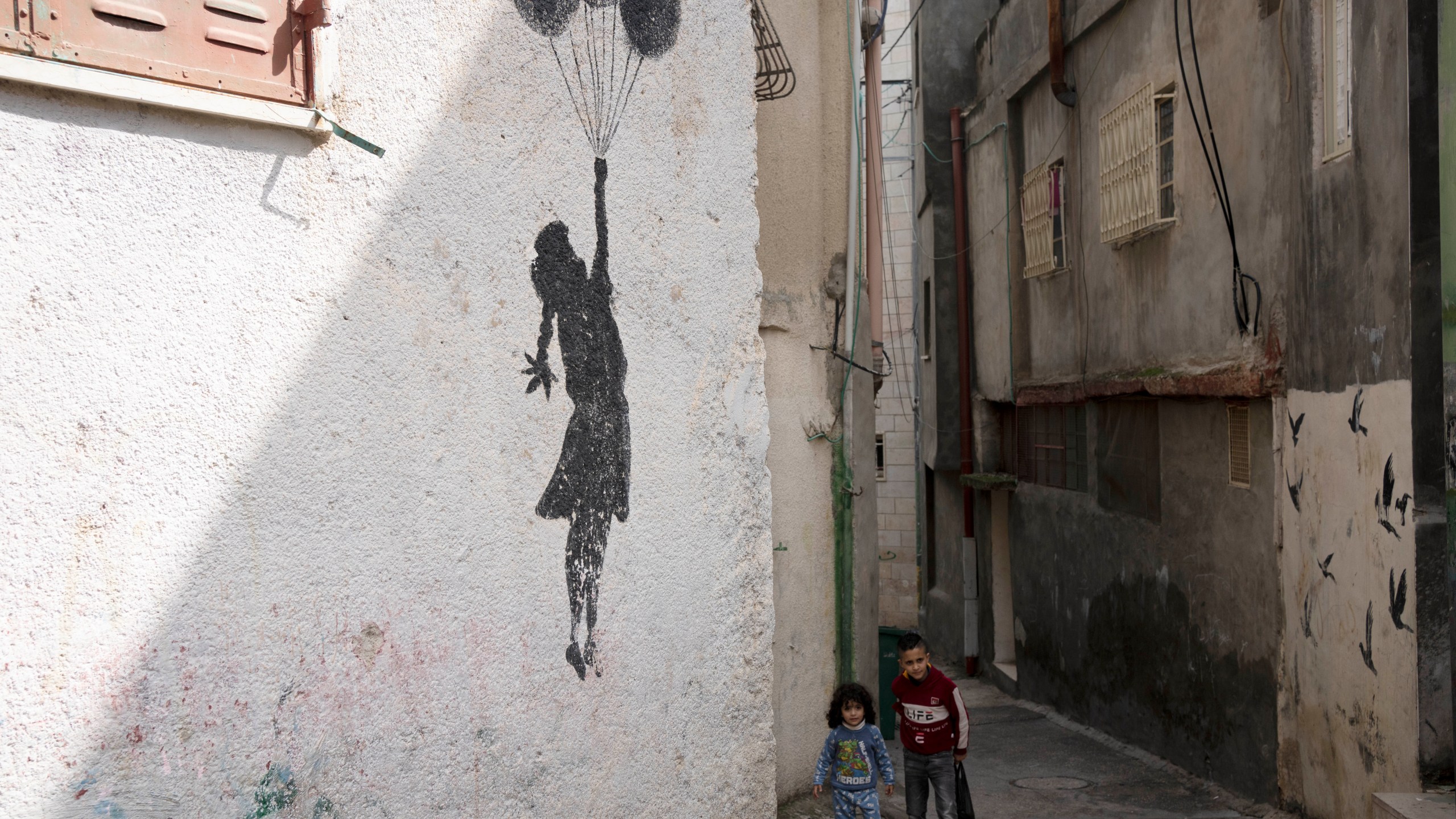 Palestinian children walk in an alley of the Aida Refugee Camp, near the health clinic and school run by the the United Nations Relief and Works Agency for Palestinian Refugees in the Near East (UNRWA) in the West Bank city of Bethlehem, Tuesday, Feb. 20, 2024. (AP Photo/Maya Alleruzzo)