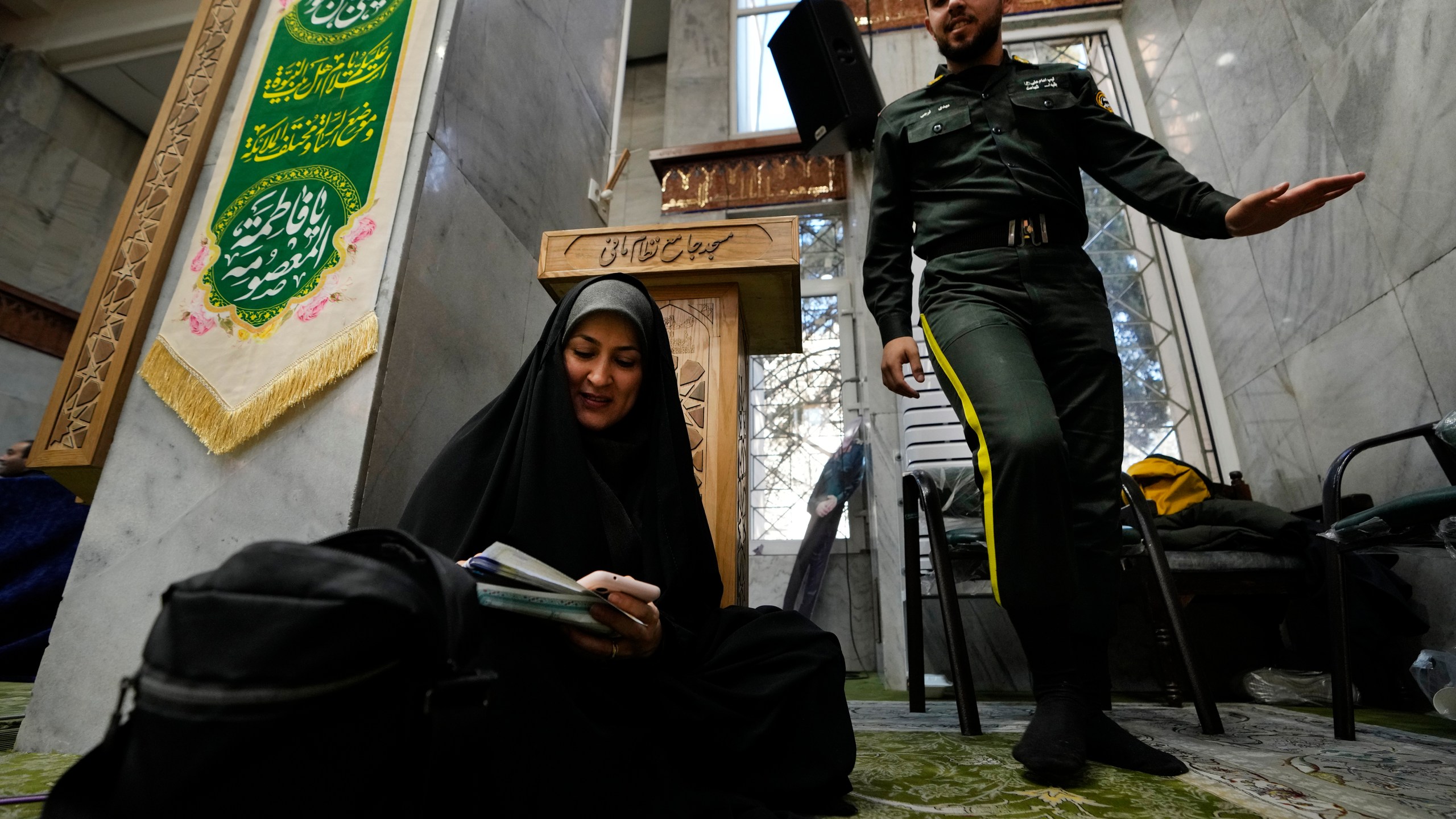 A woman fills out her ballot as a policeman walks past during the parliamentary and Assembly of Experts elections at a polling station in Tehran, Iran, Friday, March 1, 2024. Iran held the country's first election since the mass 2022 protests over mandatory hijab laws after the death in police custody of Mahsa Amini, with questions looming over just how many people will turn out at the polls. (AP Photo/Vahid Salemi)