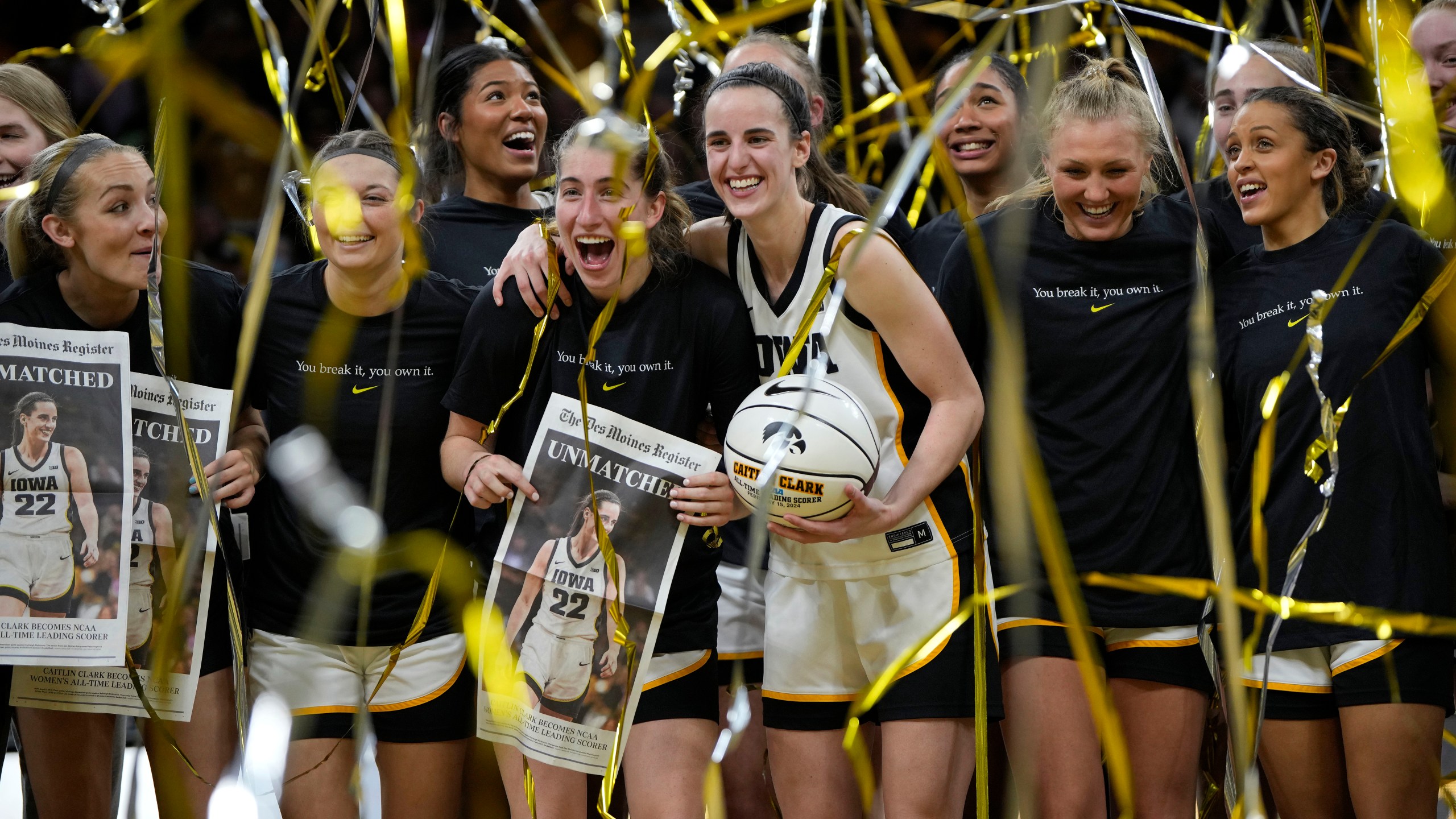 Iowa guard Caitlin Clark (22) stands with teammate after being presented with a commemorative basketball after the team's NCAA college basketball game against Michigan, Thursday, Feb. 15, 2024, in Iowa City, Iowa. Clark broke the NCAA women's career scoring record. (AP Photo/Matthew Putney)