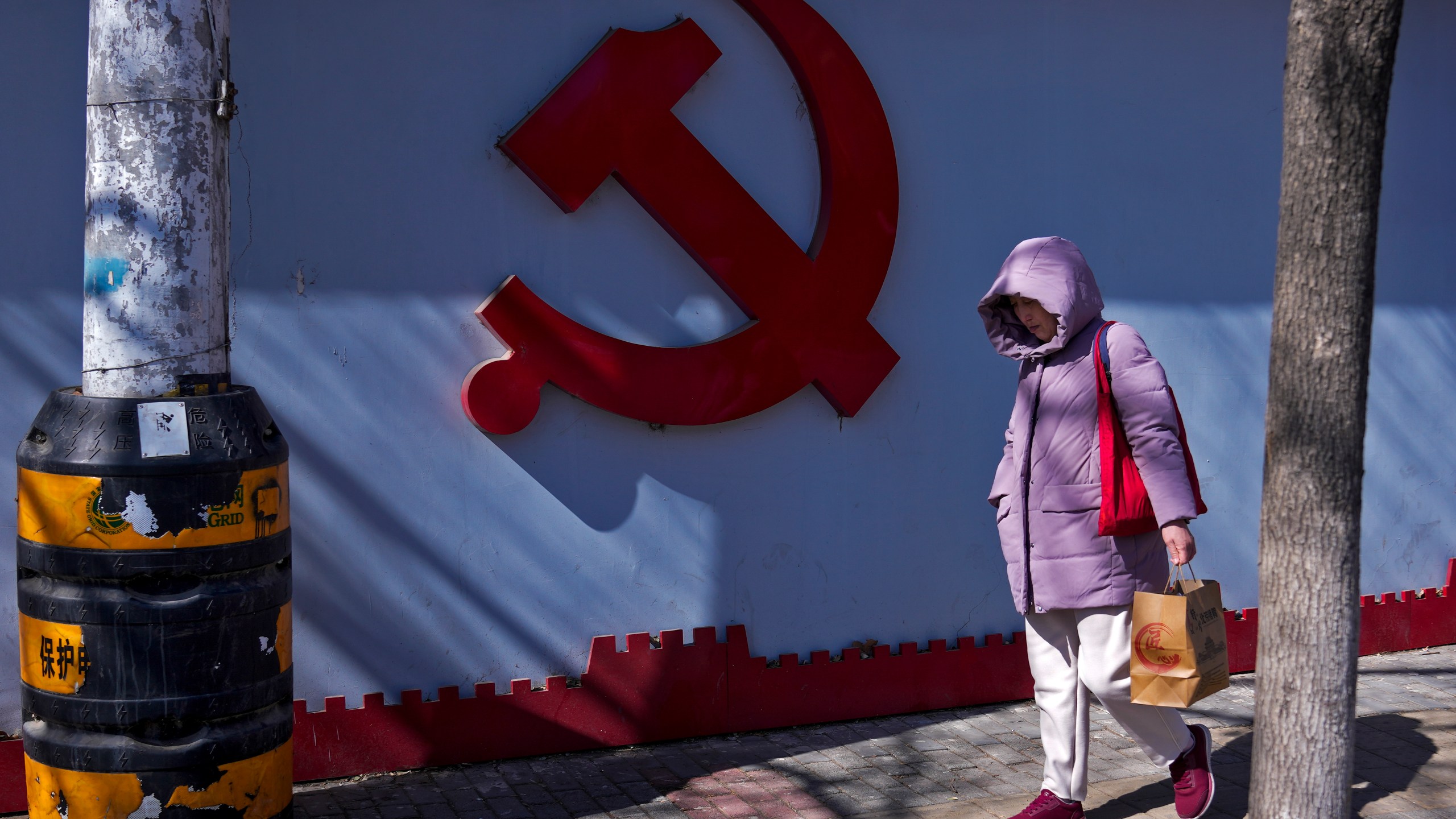 A woman walks by a Communist Party's logo on display near a residential area in Beijing on March 1, 2024. China's efforts to restore confidence and rev up the economy will top the agenda during this month’s meeting of the ceremonial national legislature. (AP Photo/Andy Wong)