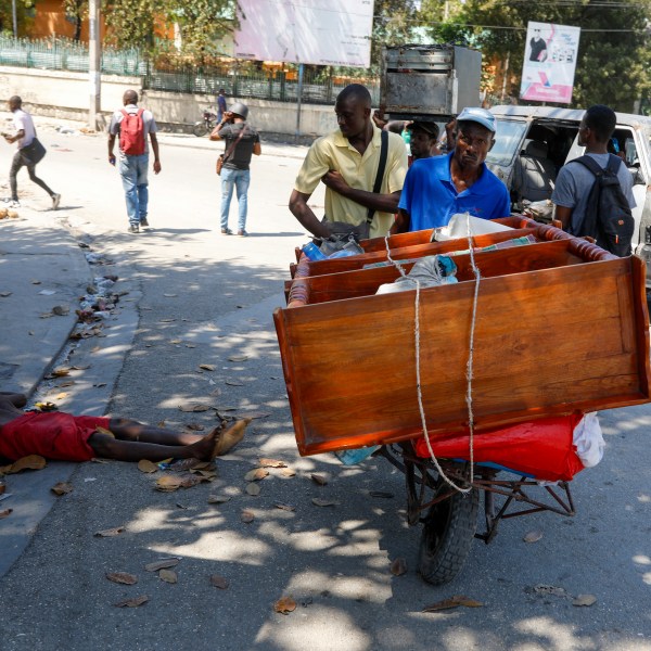 A man pushes a cart past the body of a man shot by unidentified assailants in downtown Port-au-Prince, Haiti, Monday, March 4, 2024. (AP Photo/Odelyn Joseph)