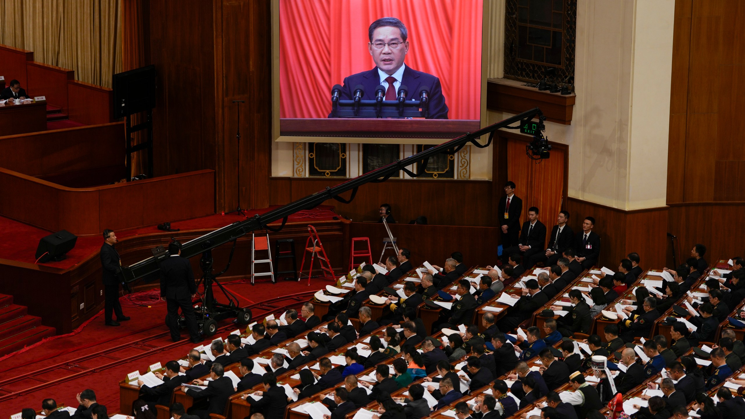 Chinese Premier Li Qiang, on screen, speaks during the opening session of the National People's Congress (NPC) at the Great Hall of the People in Beijing, China, Tuesday, March 5, 2024. (AP Photo/Ng Han Guan)