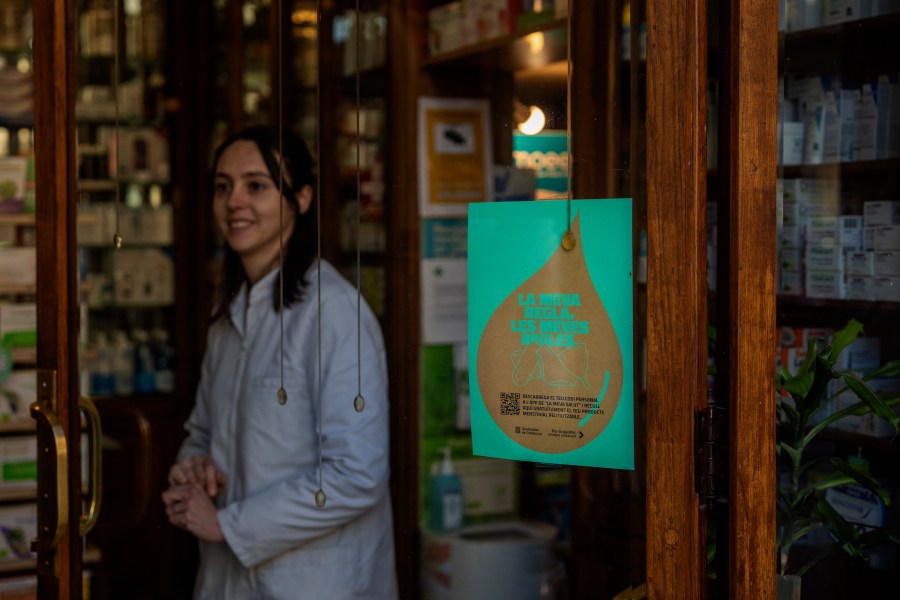 A pharmacist waits for customers next to windows where an advertisement for the new campaign of the Catalan government where you can read "my period, my rules" has been placed, inside a pharmacy in Barcelona, Spain, Tuesday, March 5, 2024. Spain's Catalonia region rolled out this week a pioneering women's health initiative that offers millions of women reusable menstruation products for free. Some 2.5 million women in northeast Spain can receive one menstrual cup, one pair of underwear for periods, and two packages of cloth pads at local pharmacies free of charge. (AP Photo/Emilio Morenatti)