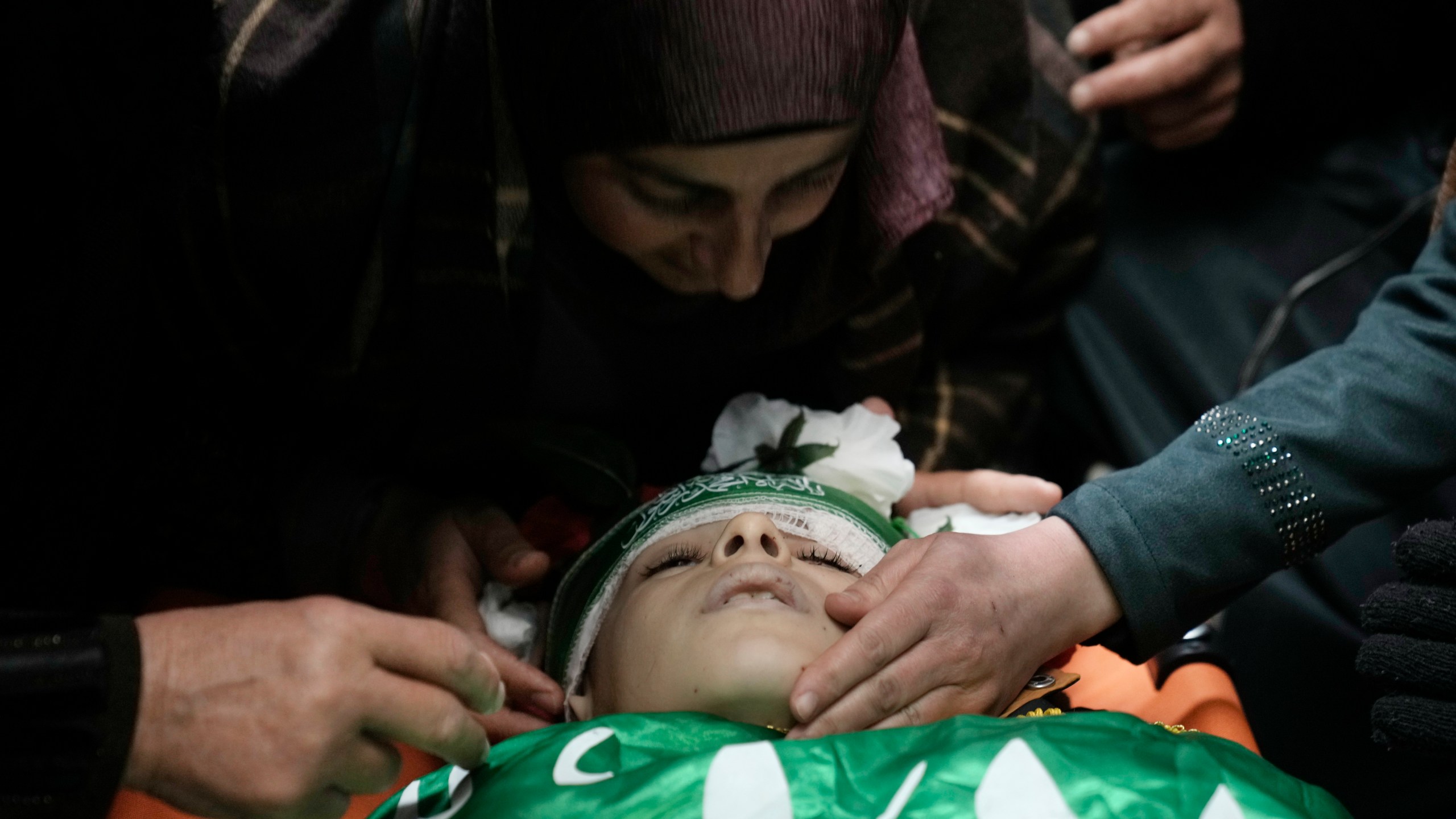 The mother of Amr al-Najjar, 11, draped in the Hamas flag, center, weeps during his funeral in the West Bank village of Burin, near Nablus, Tuesday, March 5, 2024. Palestinian media reports that he was shot during an Israeli military incursion into the village of Burin. The Israeli military says they opened fire in the village and are aware of reports of a minor being killed. (AP Photo/Majdi Mohammed)
