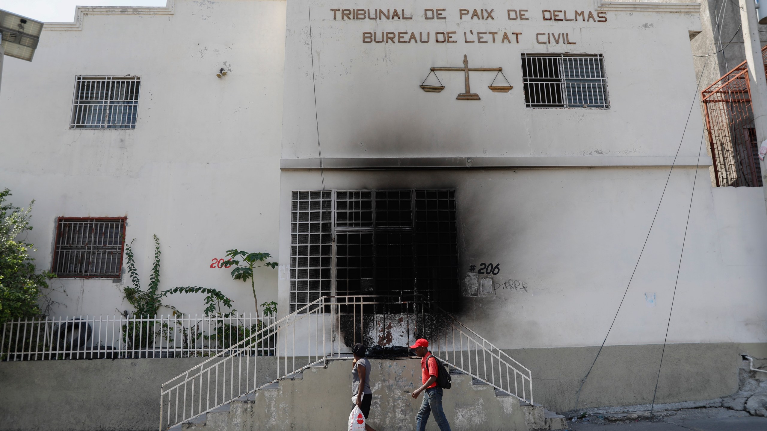 Pedestrians walk past a court building that was set on fire by gangs moments before in the Delmas 28 neighborhood of Port-au-Prince, Haiti, Wednesday, March 6, 2024. (AP Photo/Odelyn Joseph)