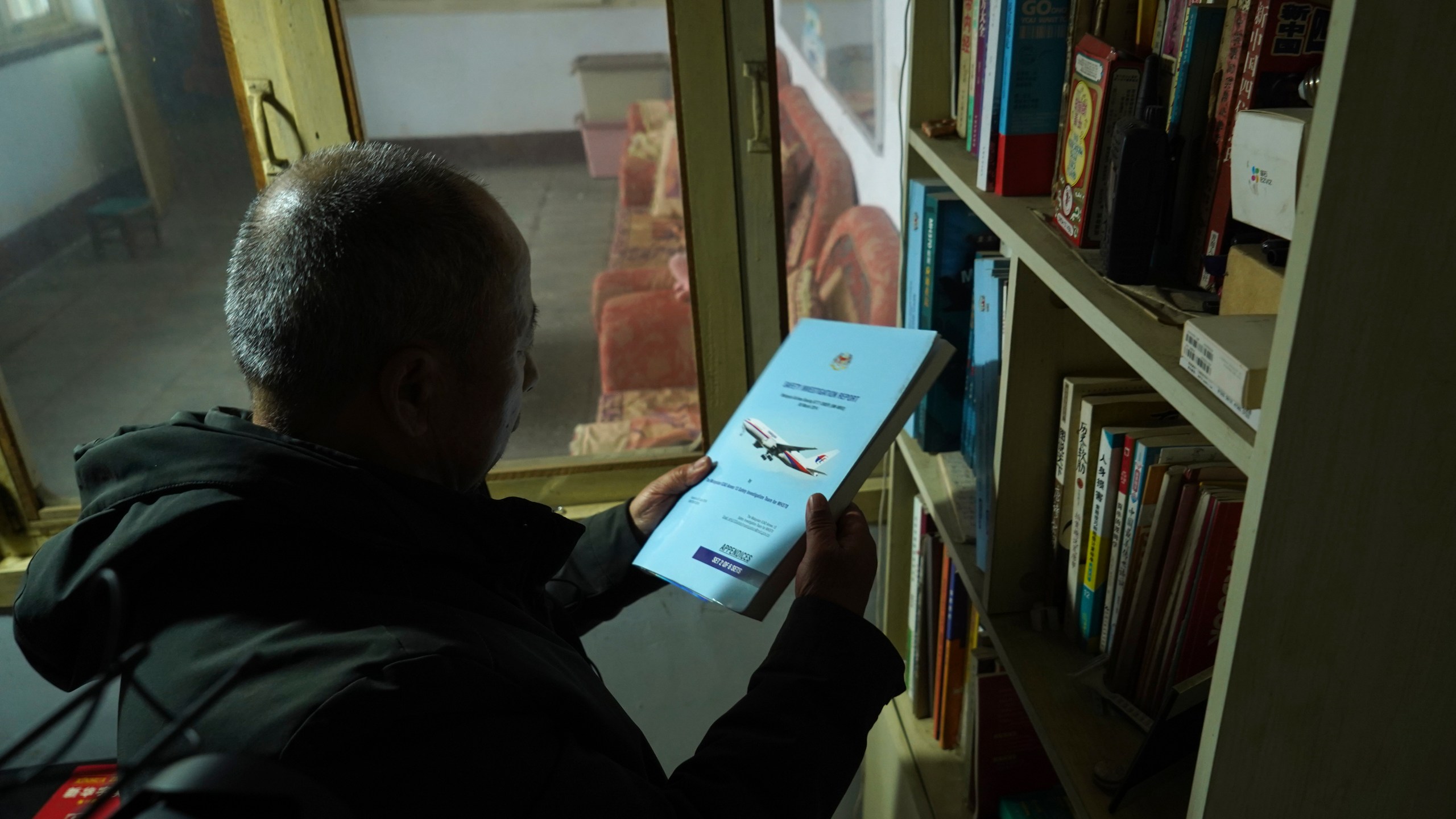 Chinese farmer Li Eryou takes an investigation report on the missing Malaysia Airlines MH370 flight from a bookshelf of his son's former room at a village in Handan in northern China's Hebei province on Feb. 28, 2024. Li, whose son was on the flight, continues to search for answers ten years on. The baffling disappearance of flight MH370 still captivates people around the world. The Boeing 777 left Kuala Lumpur with 239 people on March 8, 2014, but dropped off radar screens shortly after and never made it to Beijing, its destination. Investigators say someone deliberately shut down the plane's communications system and took the plane off course. (AP Photo/Emily Wang Fujiyama)