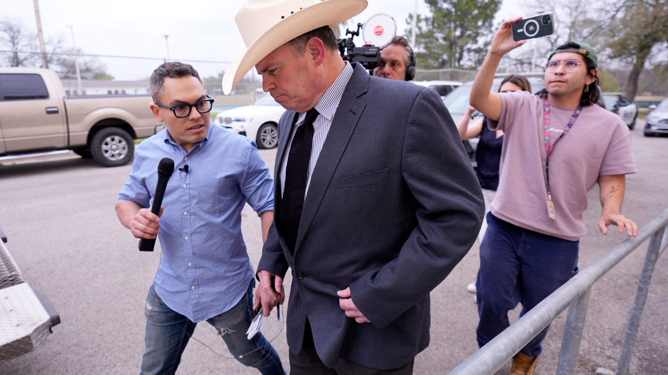 Jesse Prado, center in cowboy hat, an Austin-based investigator, is pursued by the media after he shared his findings at a special city council meeting in Uvalde, Texas, Thursday, March 7, 2024. (AP Photo/Eric Gay)