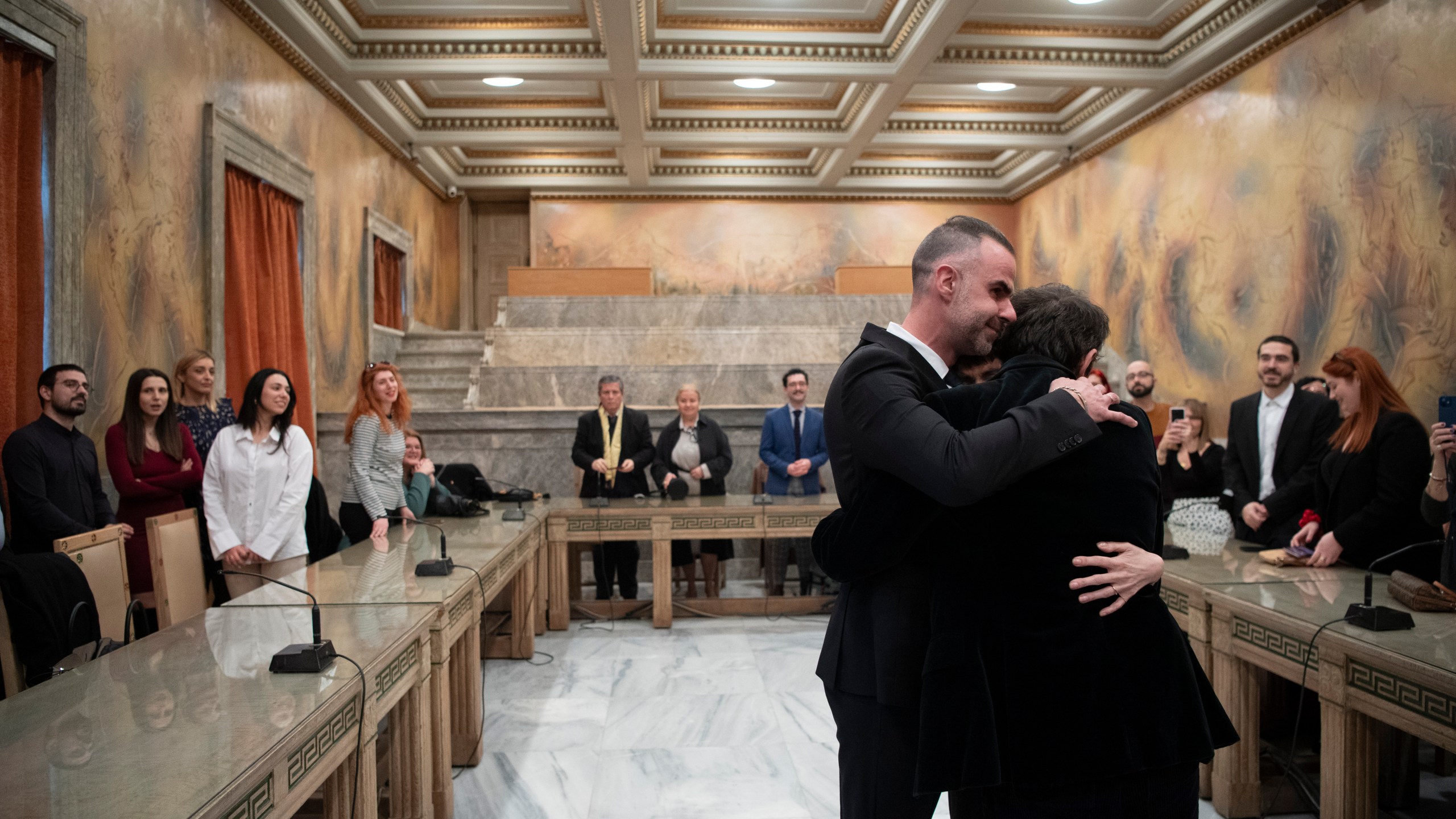 Lawyer Anastasios Samouilidis, left, hugs his husband, Greek author Petros Hadjopoulos, who uses the pen name Auguste Corteau, as guests watch, after their wedding at Athens City Hall, Greece, on Thursday, March 7, 2024. A Greek novelist and his partner on Thursday became the first male couple to be married in Athens' city hall following the legalization of same-sex marriage in Orthodox Christian Greece. (AP Photo/Michael Varaklas)