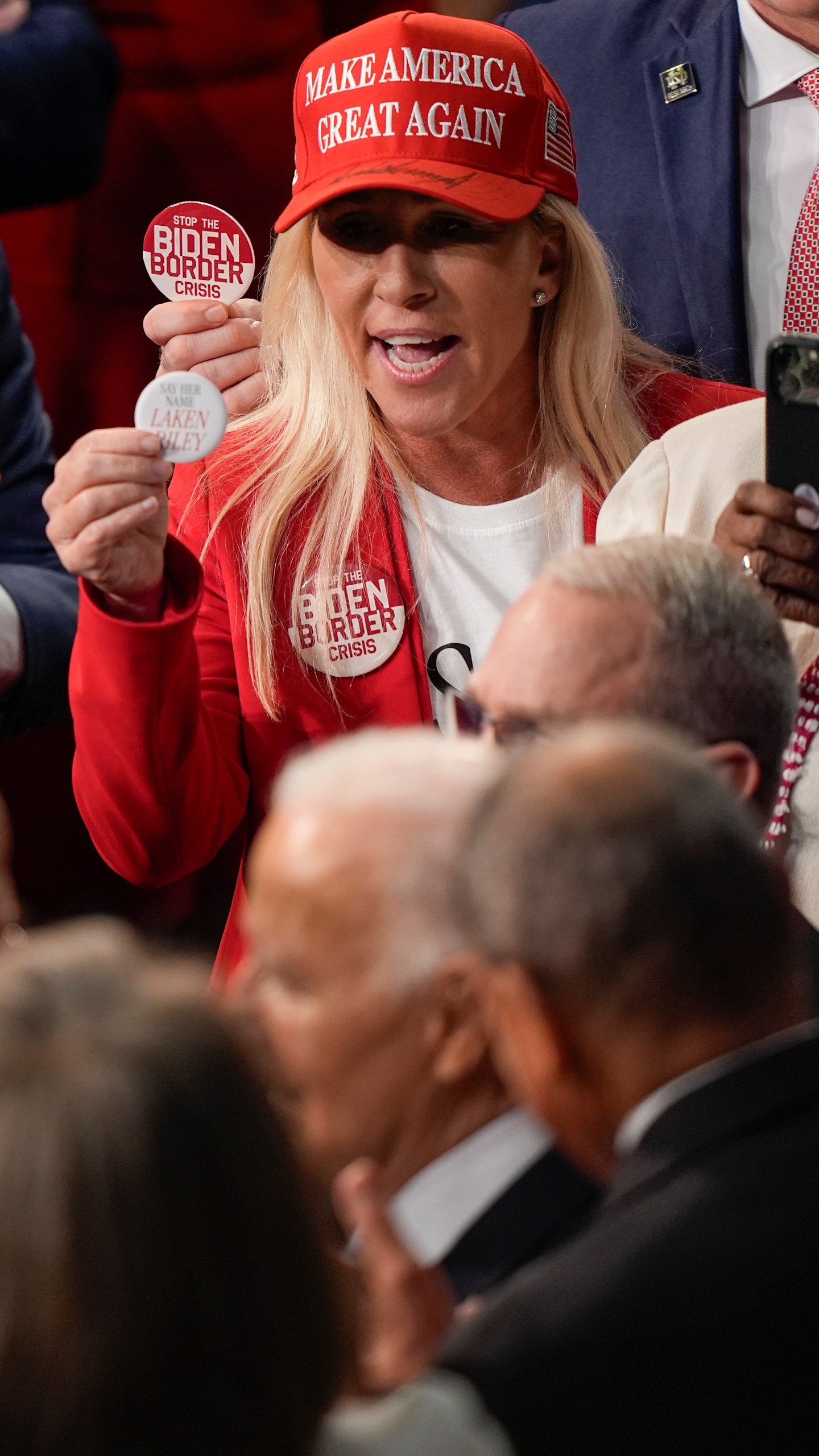 Rep. Marjorie Taylor Greene, R-Ga., top, holding up a Laken Riley button to give to President Joe Biden, bottom before the State of the Union address on Capitol Hill, Thursday, March 7, 2024, in Washington. (AP Photo/Mark Schiefelbein)