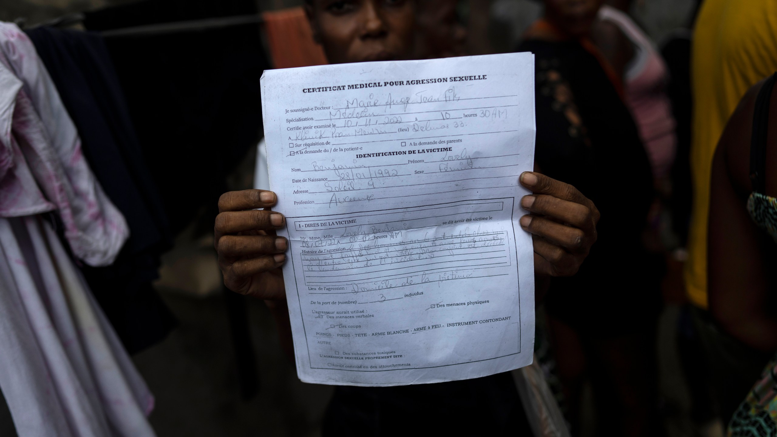 FILE - Lovely Benjamin, who was sexually assaulted by a gang member, holds up her medical report, in Jean-Kere Almicar's front yard, where she and her young son have sought refuge, in Port-au-Prince, Haiti, June 4, 2023. Gangs torched the items she used to sell, including rice and oil. While she and her 4-year-old son survived the attack in Cite Soleil, gangs killed her partner and set his body on fire. (AP Photo/Ariana Cubillos, File)