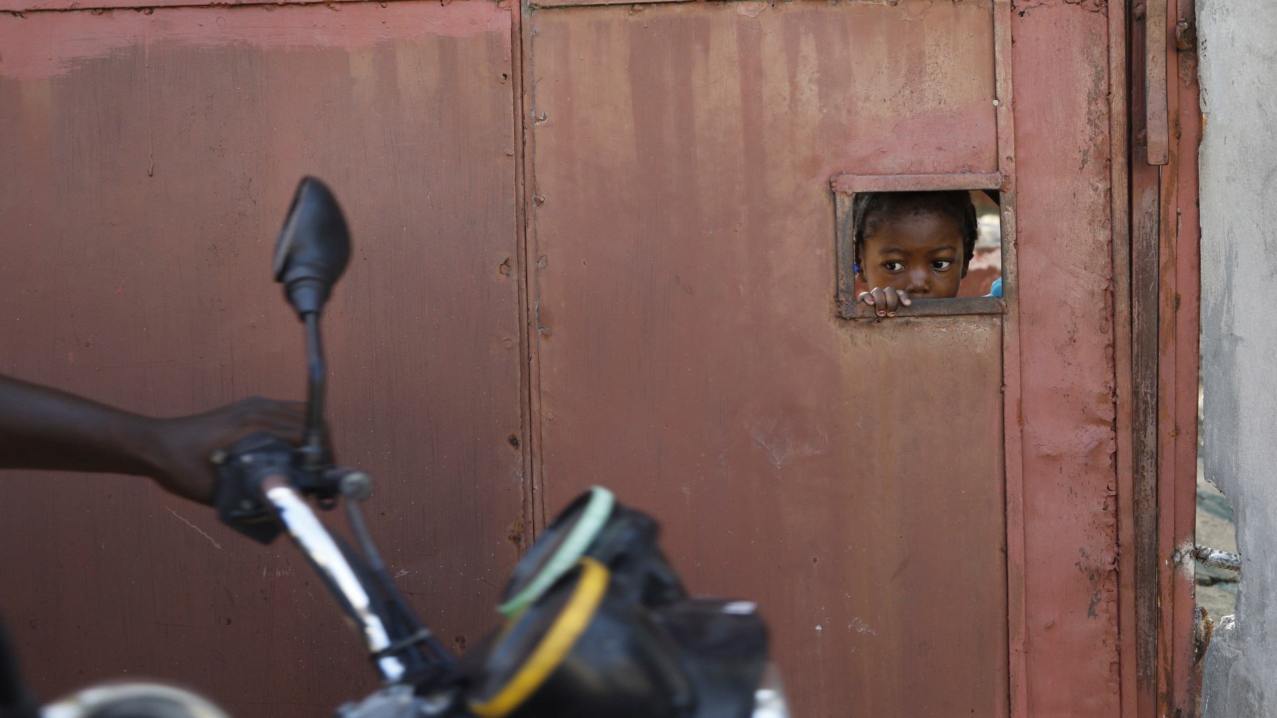 A child watches from an opening in a security gate as residents flee their homes due to gang violence, in Port-au-Prince, Haiti, Saturday, March 9, 2024. (AP Photo/Odelyn Joseph)