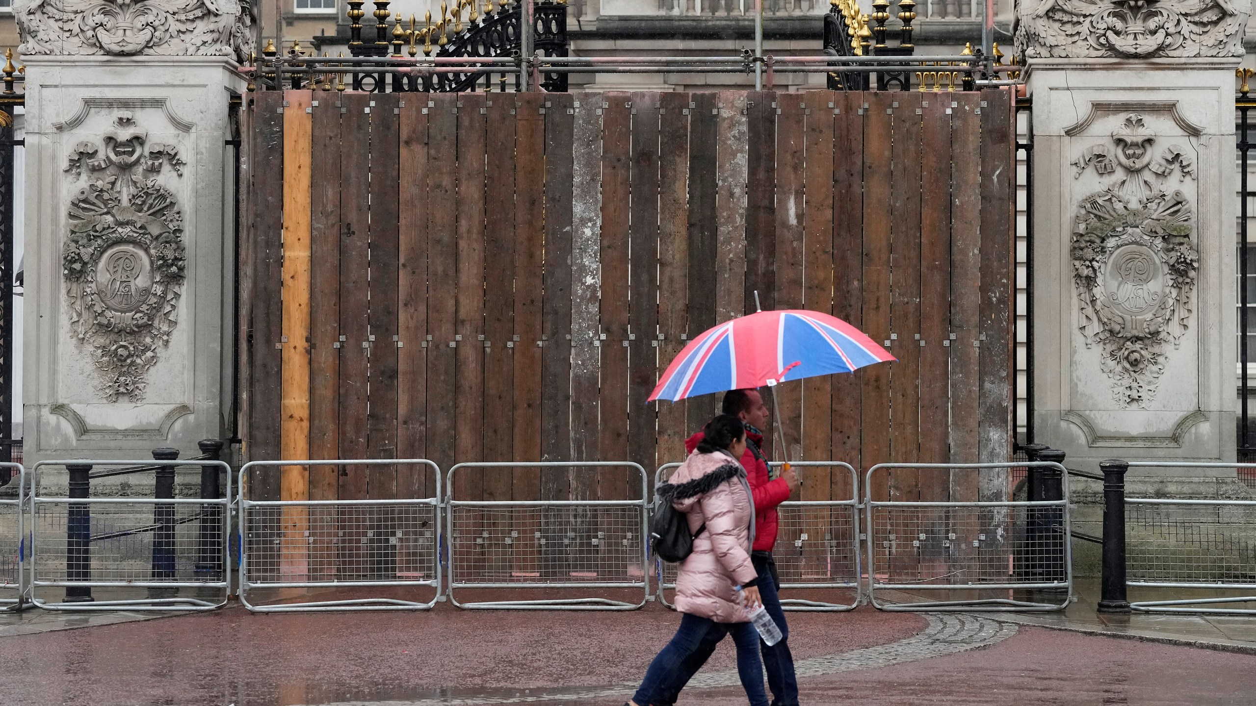 Tourists walk past boarded gates after a man was arrested after crashing his vehicle, at Buckingham Palace in London, Sunday, March 10, 2024. Armed officers arrested the man at the scene early Sunday on suspicion of criminal damage and he was taken to hospital, the Metropolitan Police said. (AP Photo/Frank Augstein)