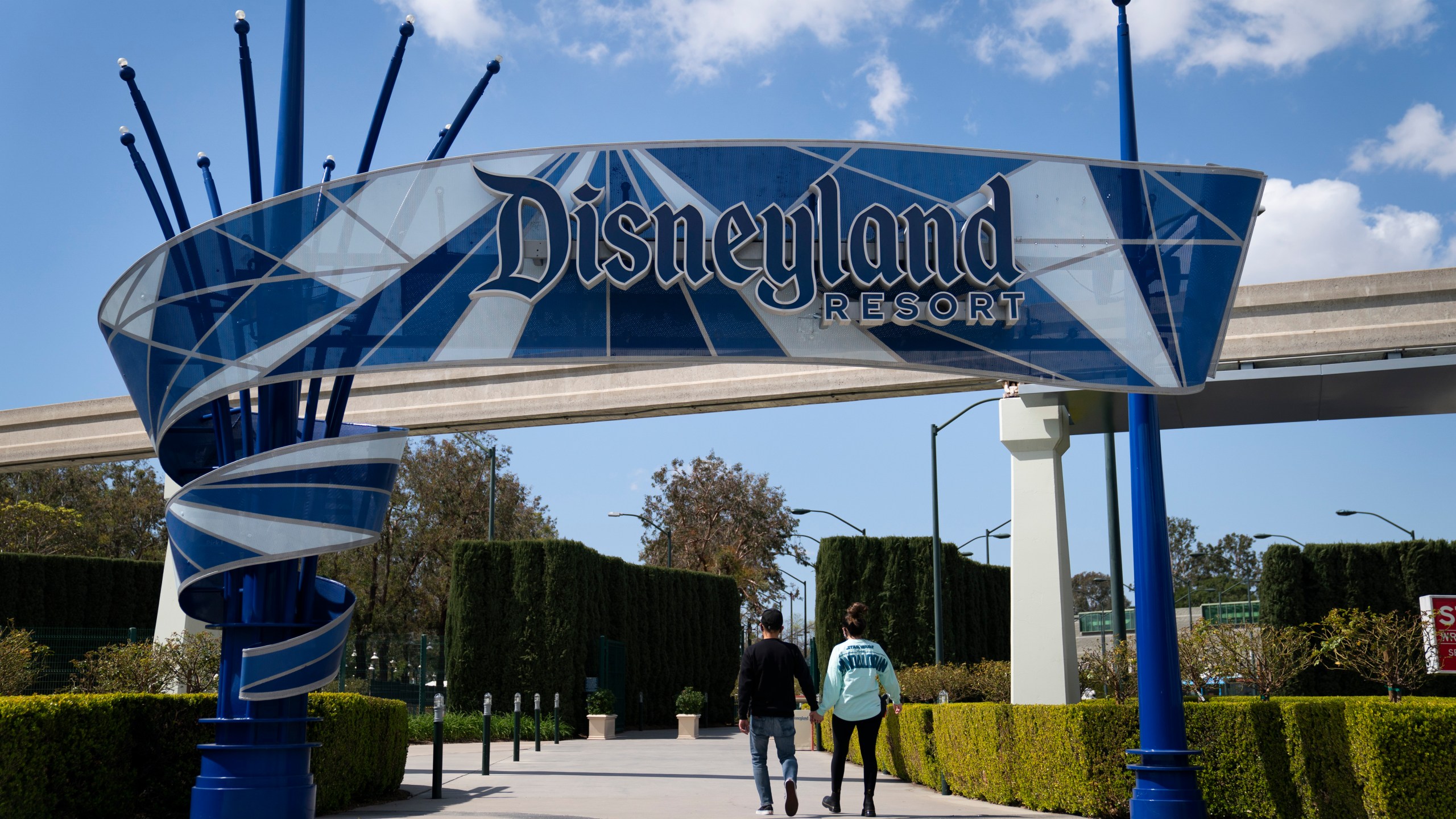 FILE - Two visitors enter Disneyland Resort in Anaheim, Calif., March 9, 2021. Disney is seeking approval from local officials to expand its California theme park offerings over the next four decades. The proposal wouldn't increase the company's geographic footprint in Anaheim, Calif., but would allow for new attractions, for example, on what is currently a large parking lot. (AP Photo/Jae C. Hong, File)