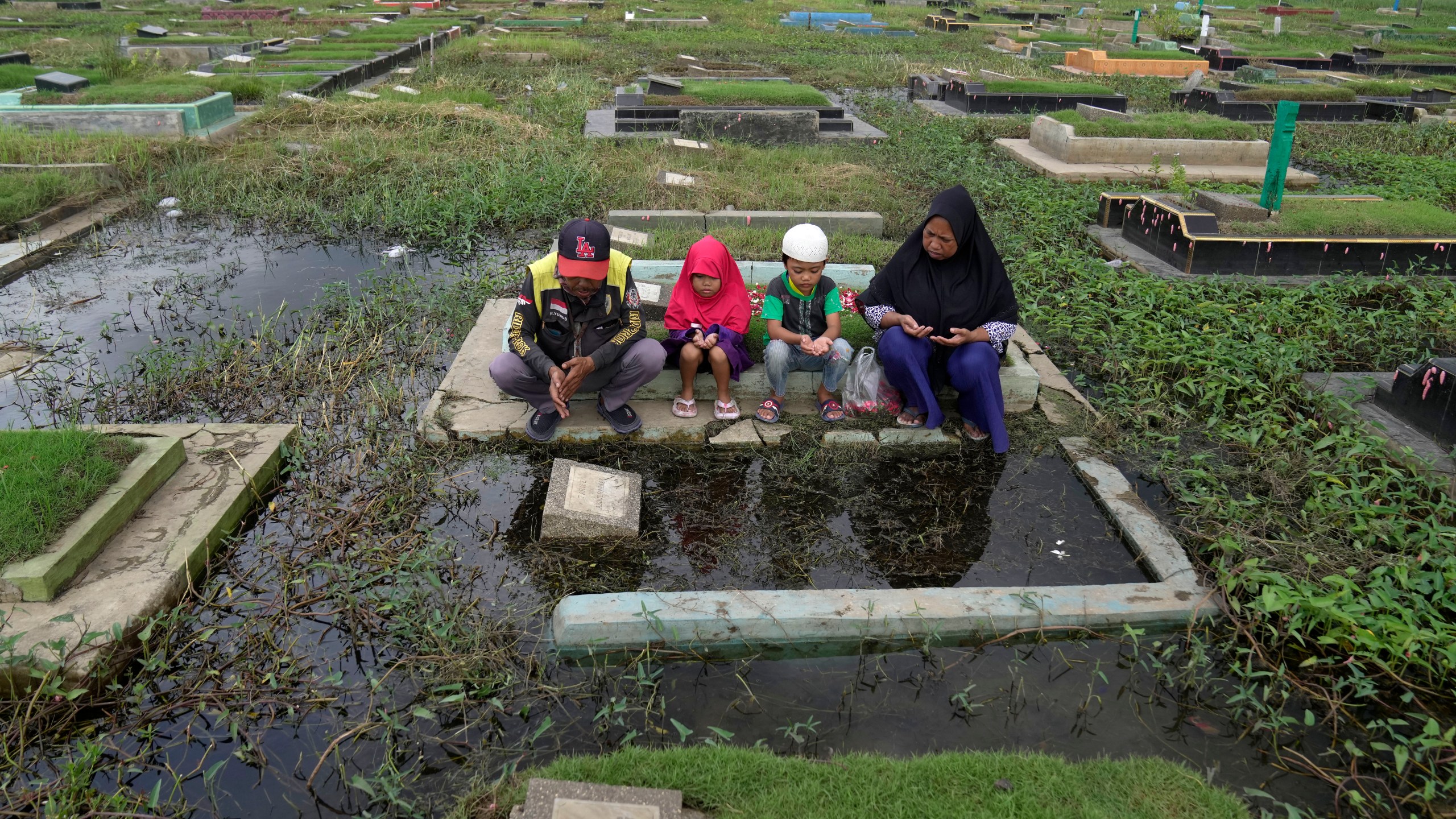 A family prays at the grave of their relative ahead of the Muslim holy fasting month of Ramadan, at a flooded cemetery in Jakarta, Indonesia, Friday, March 8, 2024. Prior Ramadan, the holiest month in Islamic calendar, Indonesian Muslims followed local tradition to visit cemeteries to pray for their deceased loved ones. (AP Photo/Dita Alangkara)