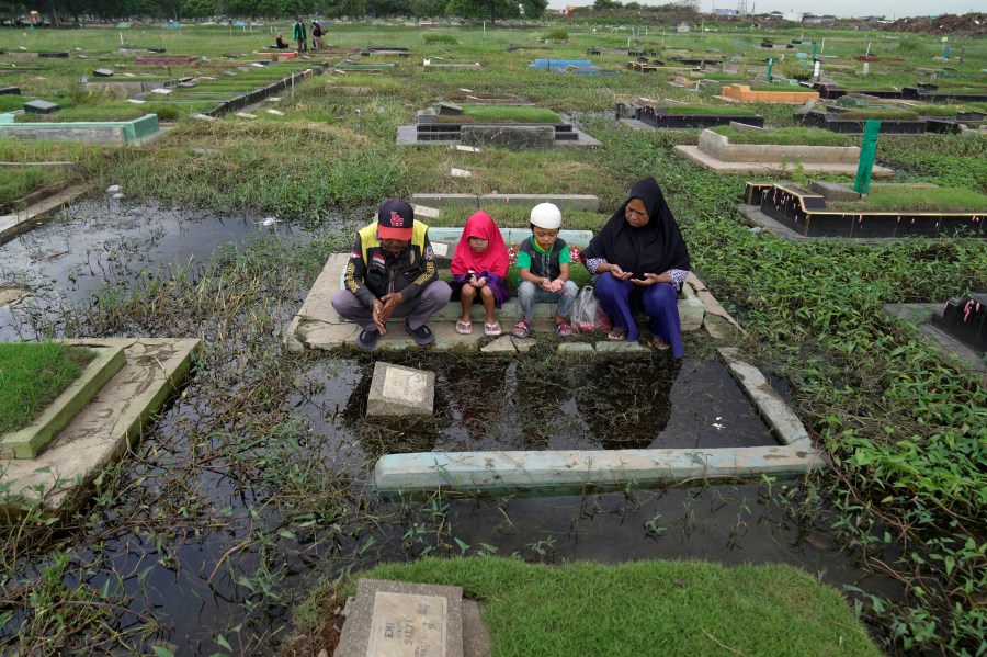 A family prays at the grave of their relative ahead of the Muslim holy fasting month of Ramadan, at a flooded cemetery in Jakarta, Indonesia, Friday, March 8, 2024. Prior Ramadan, the holiest month in Islamic calendar, Indonesian Muslims followed local tradition to visit cemeteries to pray for their deceased loved ones. (AP Photo/Dita Alangkara)