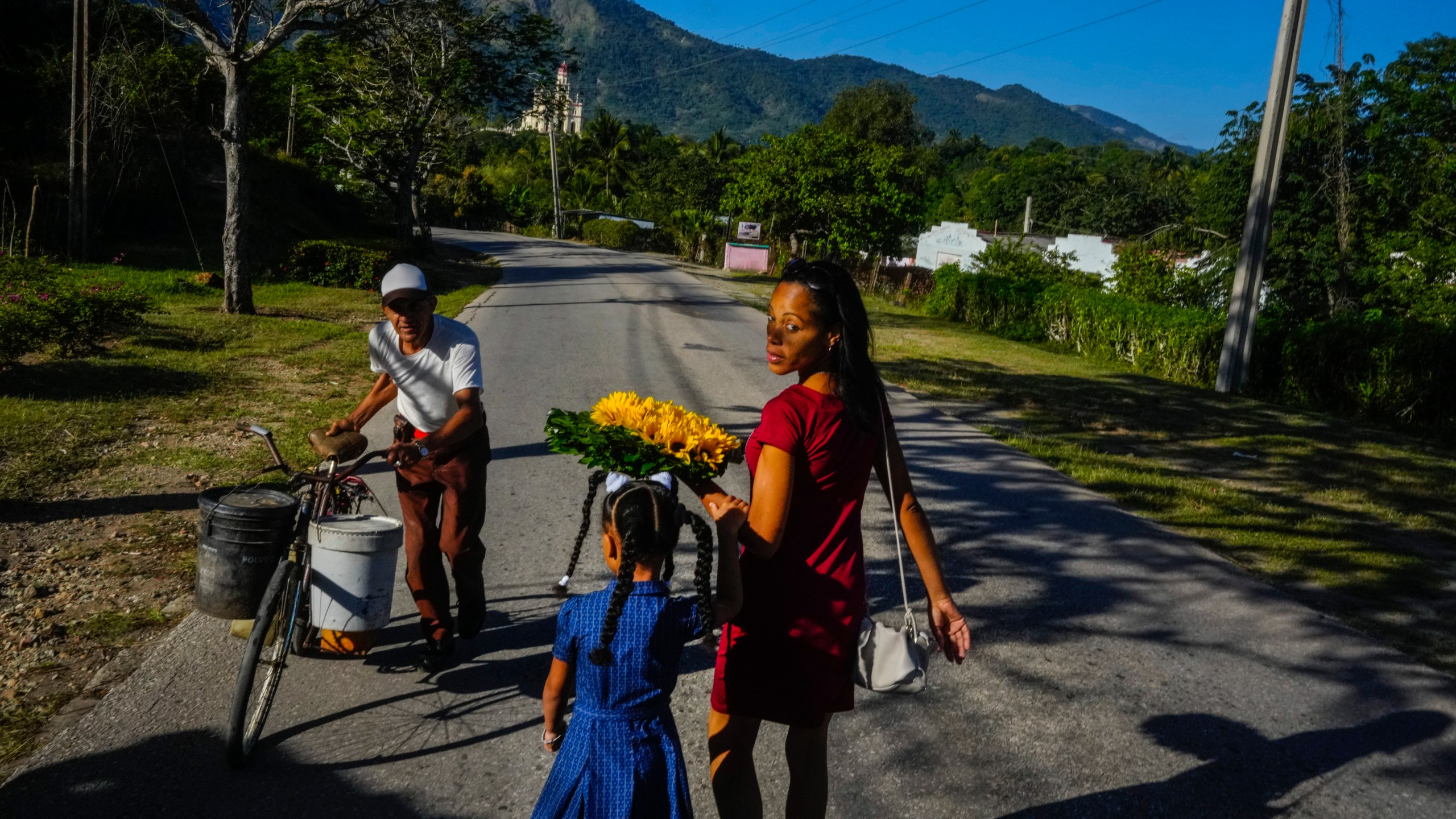 Dainet Cala and her daughter Evelyn carry flowers to leave as an offering at the shrine of the Virgin of Charity of Cobre in El Cobre, Cuba, Sunday, Feb. 11, 2024. The Vatican-recognized Virgin, venerated by Catholics and followers of Afro-Cuban Santeria traditions, is at the heart of Cuban identity, uniting compatriots from the Communist-run Caribbean island to those who were exiled or emigrated to the U.S. (AP Photo/Ramon Espinosa)