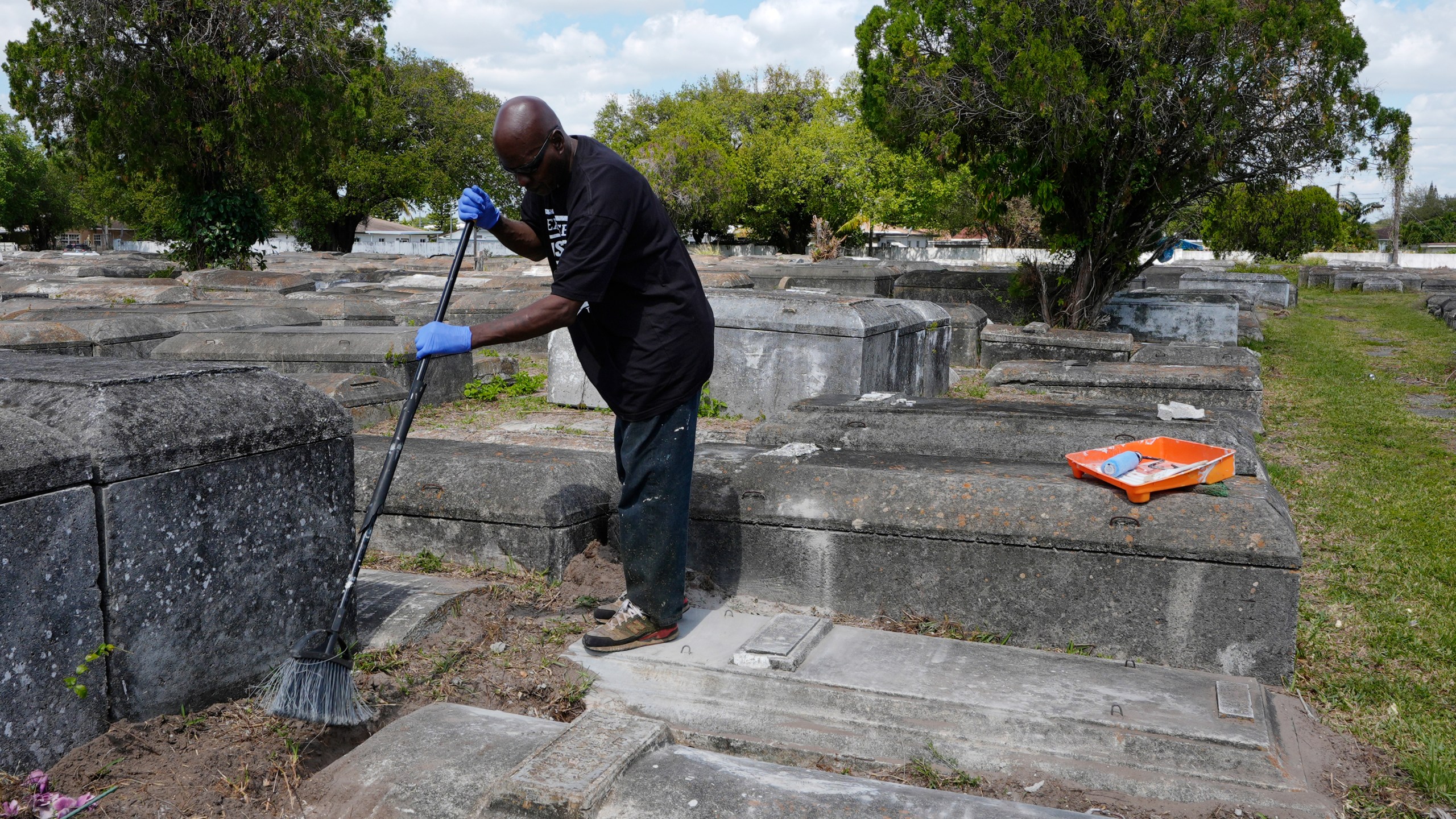 Frank Wooden sweeps the graves of a local family at the Lincoln Memorial Park Cemetery, Monday, Feb. 26, 2024, in the Brownsville neighborhood of Miami. Wooden became the caretaker after his brother, Jessie, purchased the historically segregated Black cemetery where their mother is buried. “When we got here it looked like a jungle,” Frank Wooden said. “Some people had to jump the fence to get in to see their loved one.” (AP Photo/Marta Lavandier)