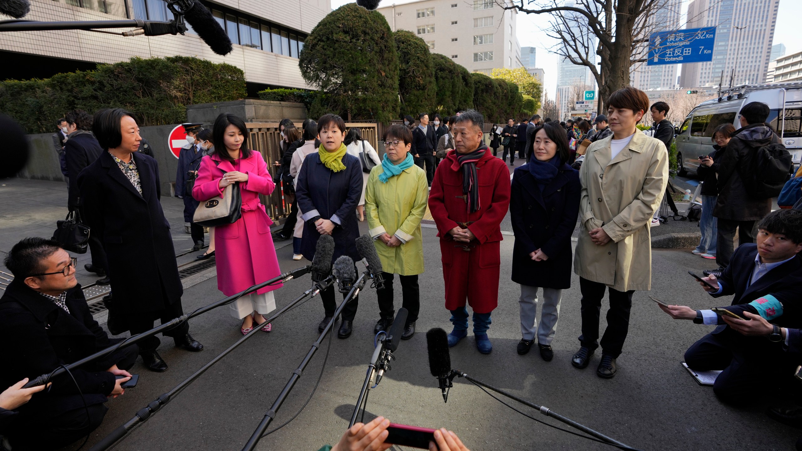 One of the plaintiffs, with a green scarf, fourth left, speaks before media members by the main entrance of the Tokyo district court before hearing the ruling regarding LGBTQ+ marriage rights, in Tokyo, Thursday, March 14, 2024. The Japanese court on Thursday ruled that not allowing same-sex couples the same marital benefits as heterosexuals violates their fundamental right to have a family, but the current civil law did not take into consideration sexual diversity and is not clearly unconstitutional, a partial victory for Japan's LGBTQ+ community calling for equal marriage rights.(AP Photo/Hiro Komae)