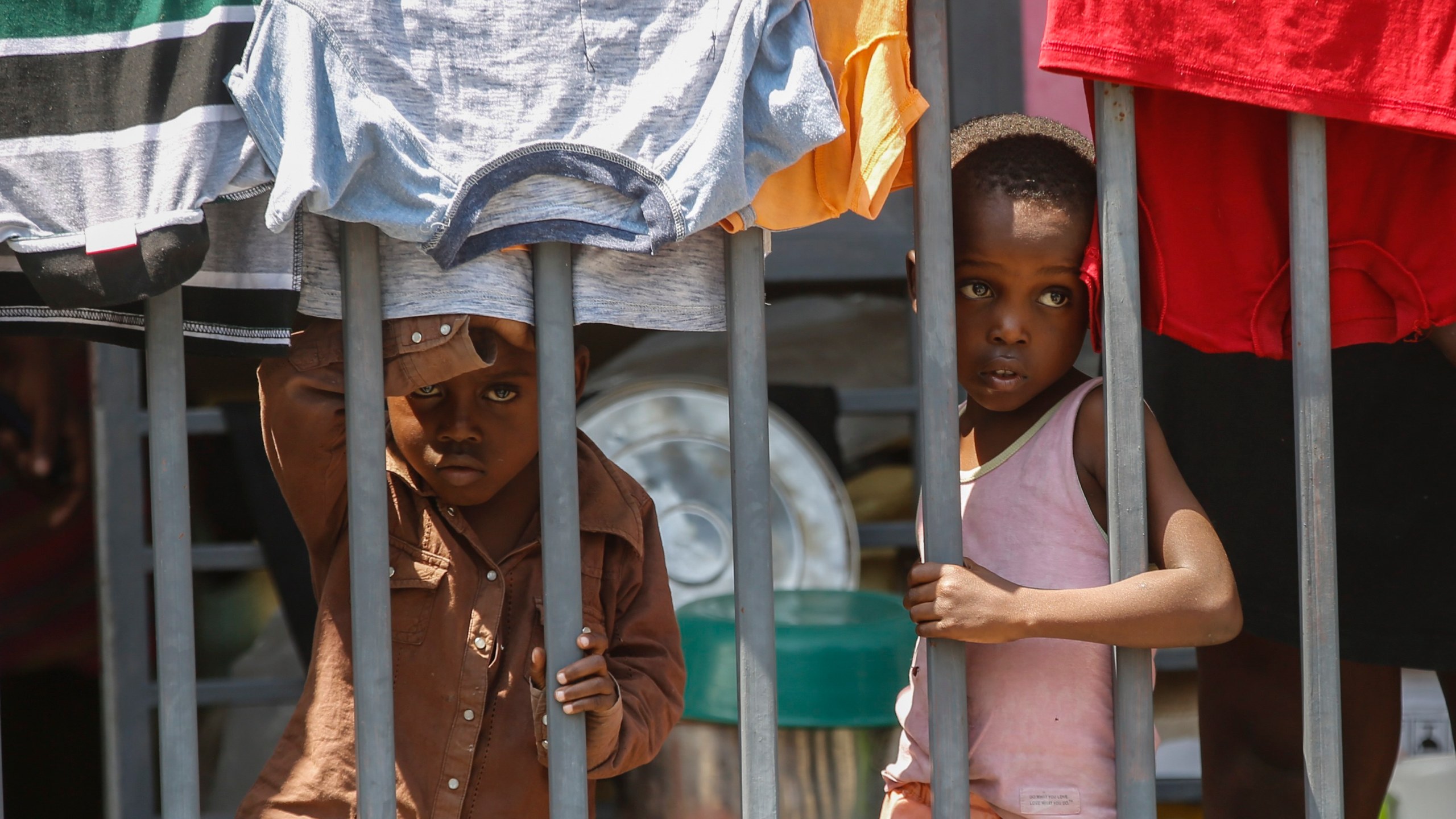 Children look through a fence at a shelter for families displaced by gang violence, in Port-au-Prince, Haiti, Wednesday, March 13, 2024. (AP Photo/Odelyn Joseph)