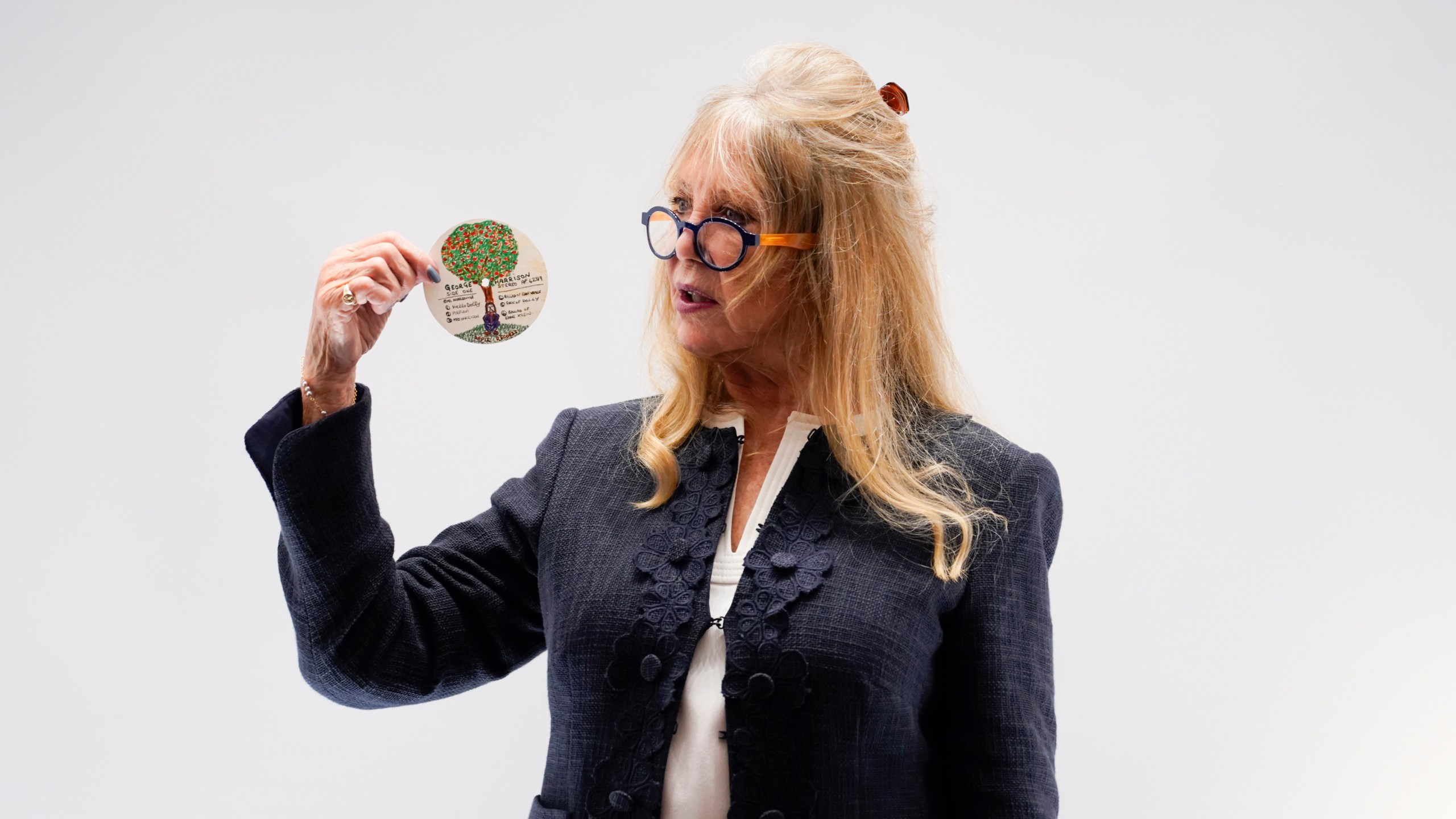 Pattie Boyd holds an original designed doodle by George Harrison as part of The Pattie Boyd Collection at Christie's, in London, Thursday, March 14, 2024. The doodle is estimated to sell £3,000-5,000. (AP Photo/Alberto Pezzali)