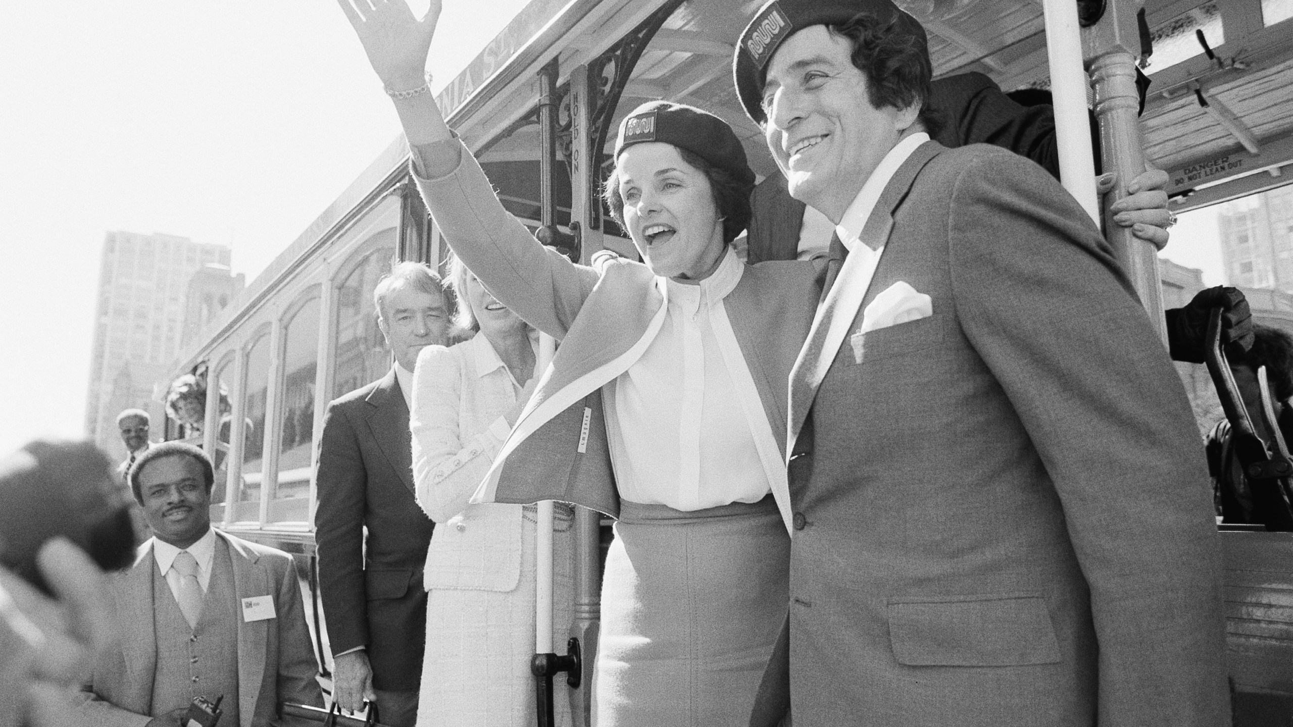FILE - San Francisco Mayor Dianne Feinstein and singer Tony Bennett, who sang " I Left My Heart in San Francisco," hangs on to the outside of a cable car in San Francisco before taking a test ride, May 2, 1984. Bennett loved San Francisco and its cable cars and in return, the city has dedicated one of those cable cars to the famous crooner, who died in July 2023. Cable car 53, built in 1907, has several plaques and painted gold ribbons remembering Bennett. (AP Photo/Jeff Reinking, File)