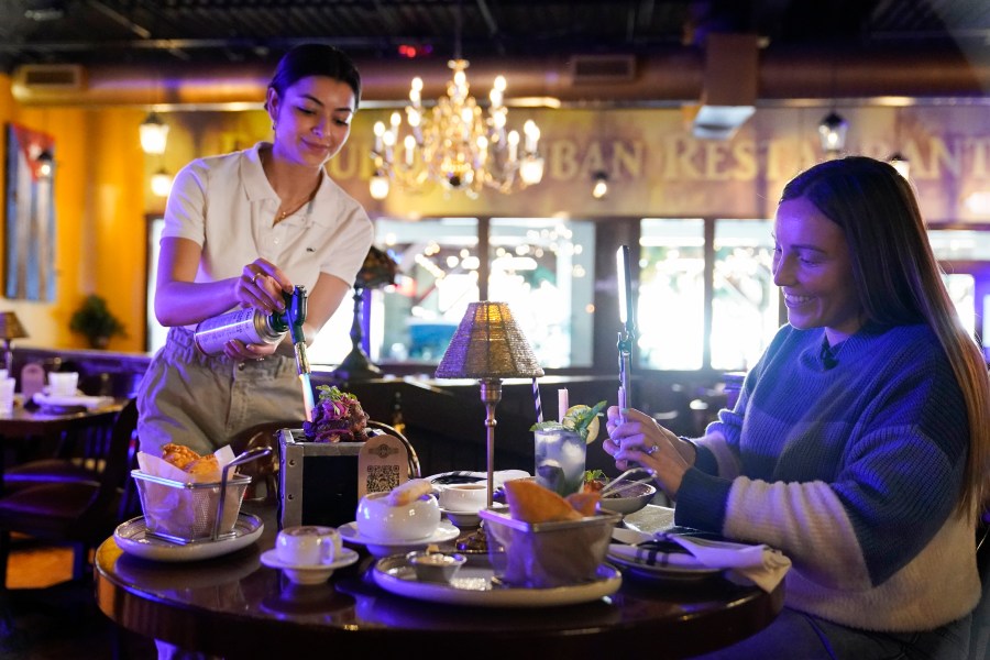 Restaurant owner Ana Acela Perez, left, assists content creator Jensen Savannah, with a video for her business at El Puro Cuban Restaurant, Thursday, March 14, 2024, in Charlotte, N.C. (AP Photo/Erik Verduzco)