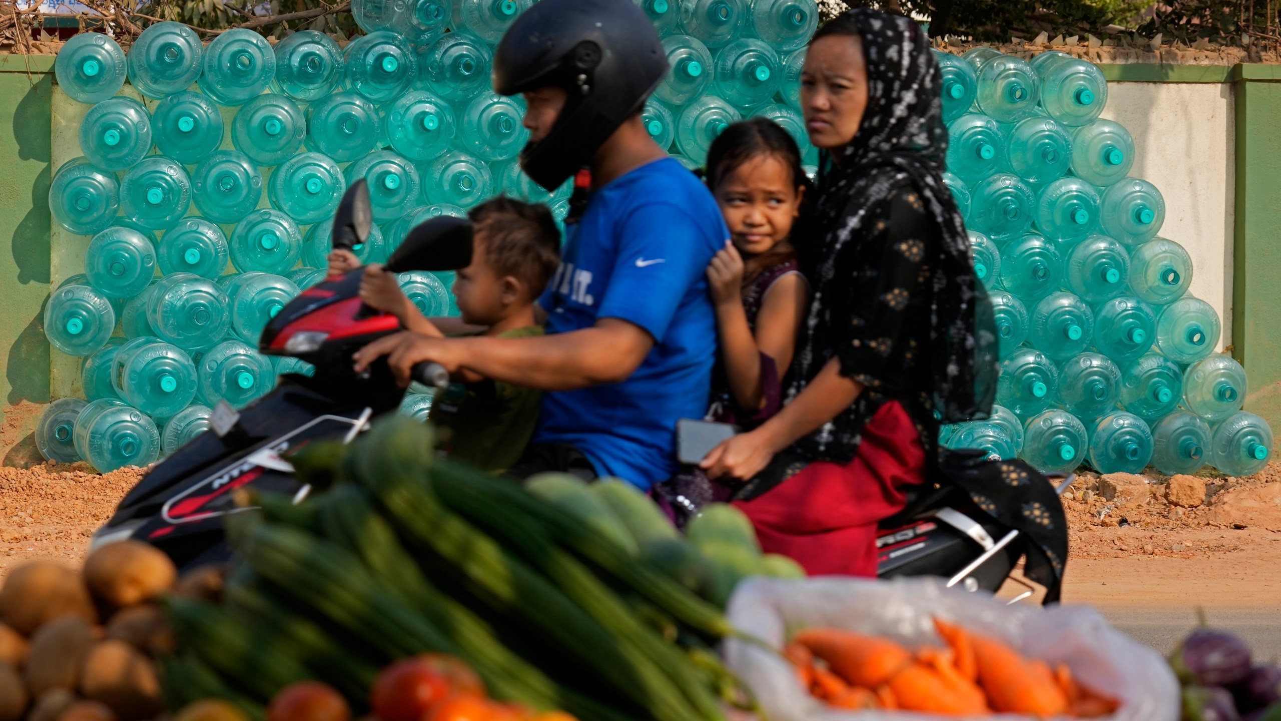 A motorist rides with his family past the stacked empty drinking water cans to be transported for refilling in Bengaluru, India, Monday, March 11, 2024. (AP Photo/Aijaz Rahi)
