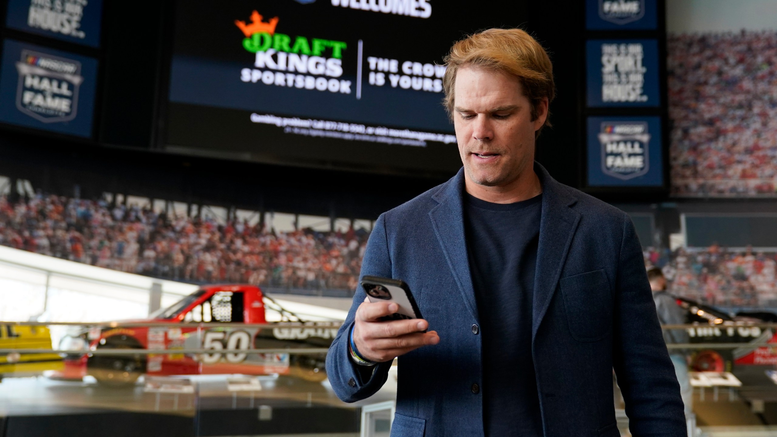 FILE - Fox Sports broadcaster Greg Olsen retrieves his receipt after placing the first ceremonial bet in North Carolina during a DraftKings event celebrating the launch of mobile and online sports wagering across the state at the NASCAR Hall of Fame, Monday, March 11, 2024, in Charlotte, N.C. As March Madness gets underway, more people than ever now can legally bet on sports. A total of 38 states and the District of Columbia now allow some form of sports betting.(AP Photo/Erik Verduzco, File)