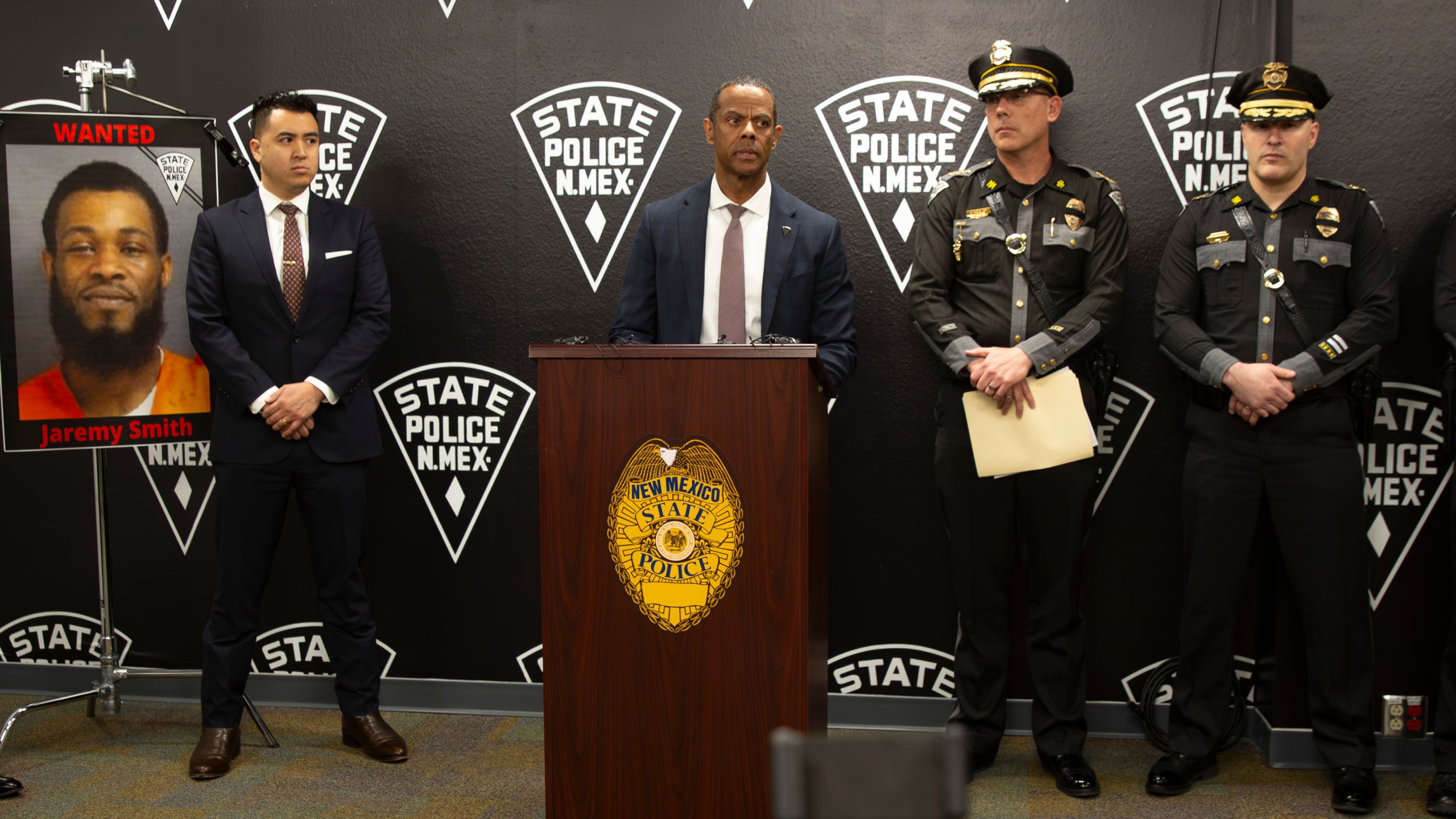 A portrait of Jaremy Smith is displayed beside U.S. Attorney for New Mexico Alexander Uballez, left, on Saturday, March 16, 2024, as Public Safety Secretary Jason Bowie gives a briefing following the death of New Mexico State Police officer Justin Hare, in Albuquerque, N.M. The suspect in the shooting death of a state police officer has been captured in a Sunday-morning, March 17, confrontation on the west side of Albuquerque, the New Mexico State Police announced Sunday. (Jon Austria/The Albuquerque Journal via AP)