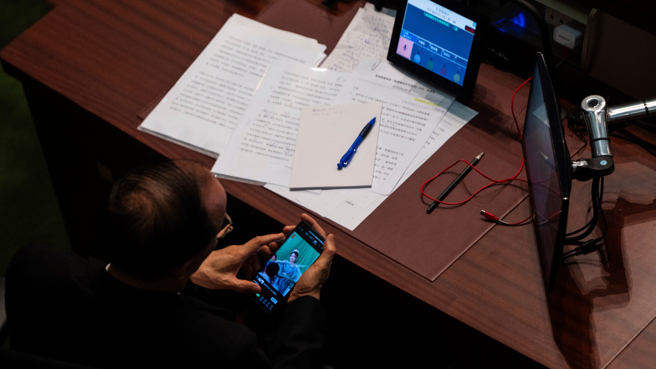 A lawmaker watches his phone during the second reading of the Basic Law Article 23 legislation at the Legislative Council in Hong Kong, Tuesday, March 19, 2024. (AP Photo/Louise Delmotte)