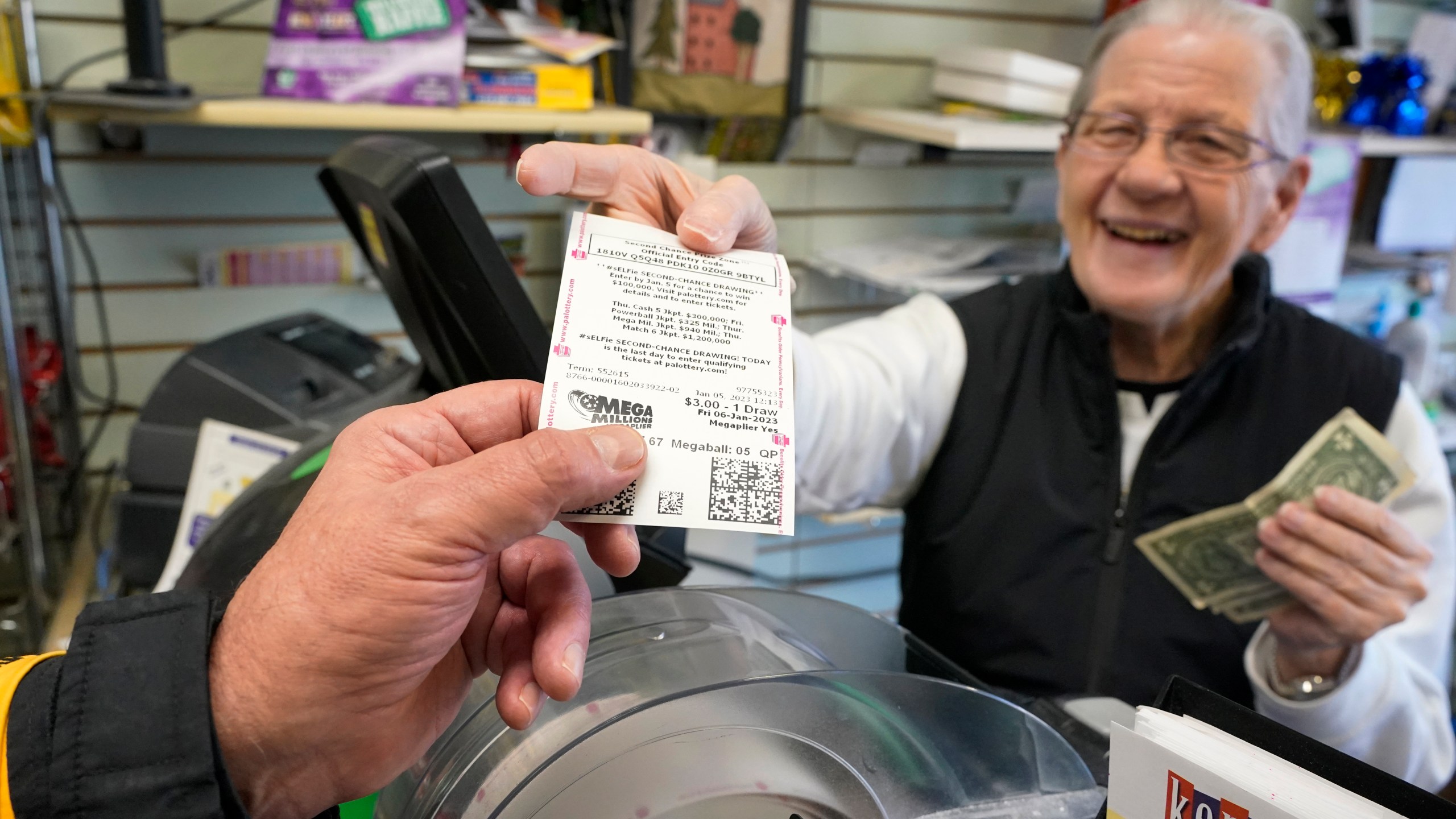 FILE - Dot Skoko, owner of Dot's Dollar More or Less shop in Mt. Lebanon, Pa., hands a customer a Mega Millions lottery ticket, Thursday, Jan. 5, 2022. The Mega Millions jackpot has reached an astounding $977 million for Friday night’s drawing after no tickets matched all six numbers drawn on Tuesday night. (AP Photo/Gene J. Puskar, File)
