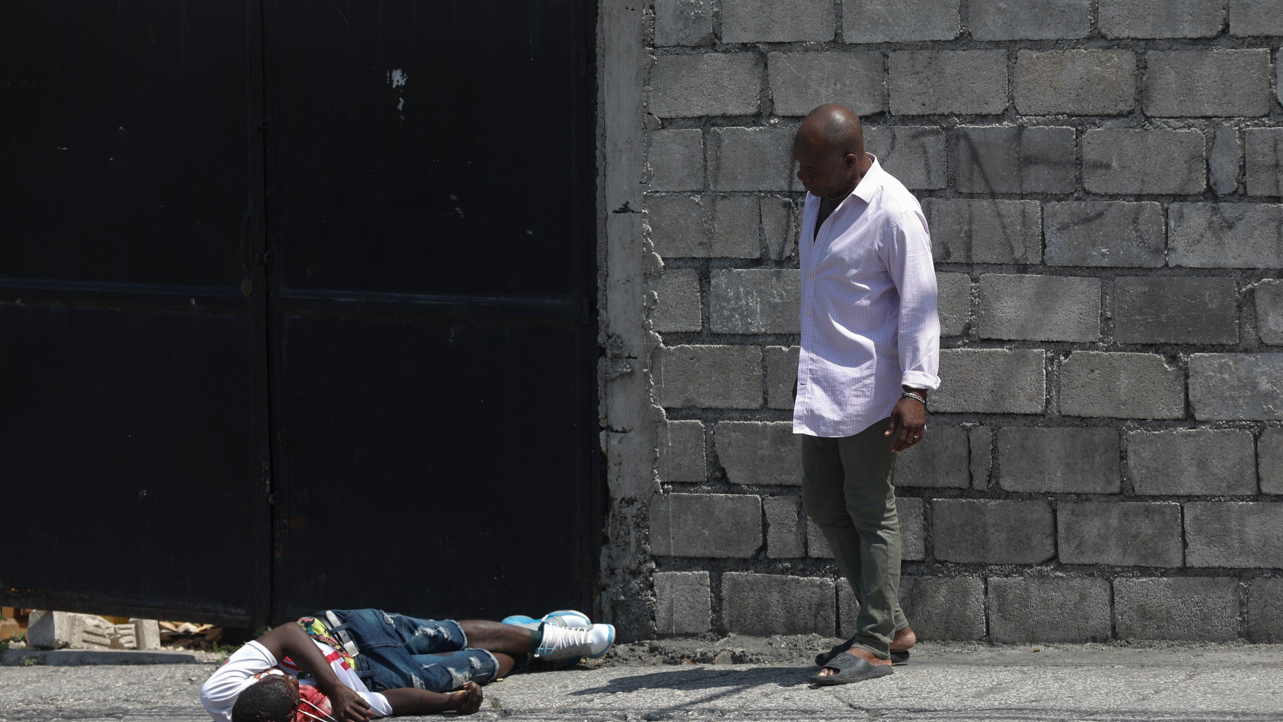 A resident looks at a body lying in the street in the Delmas area of Port-au-Prince, Haiti, Wednesday, March 20, 2024. The red item next to the body is a cell phone. (AP Photo/Odelyn Joseph)