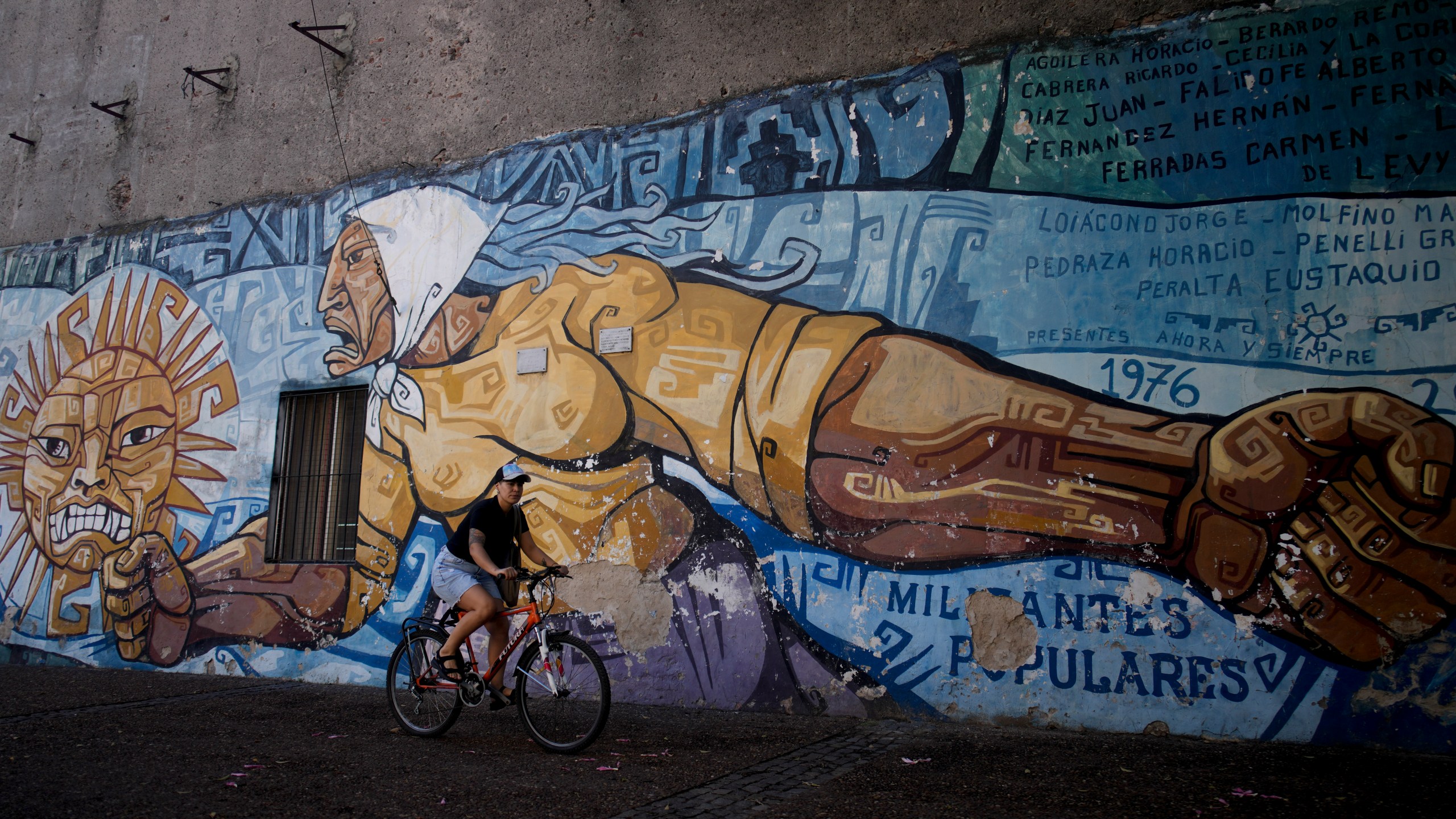 A cyclist rides past a mural honoring the Mothers of Plaza de Mayo in Buenos Aires, Argentina, Tuesday, March 19, 2024. The Mothers of Plaza de Mayo is a human rights organization created by women whose children were kidnapped by the military dictatorship that ruled Argentina from 1976 to 1983. (AP Photo/Natacha Pisarenko)