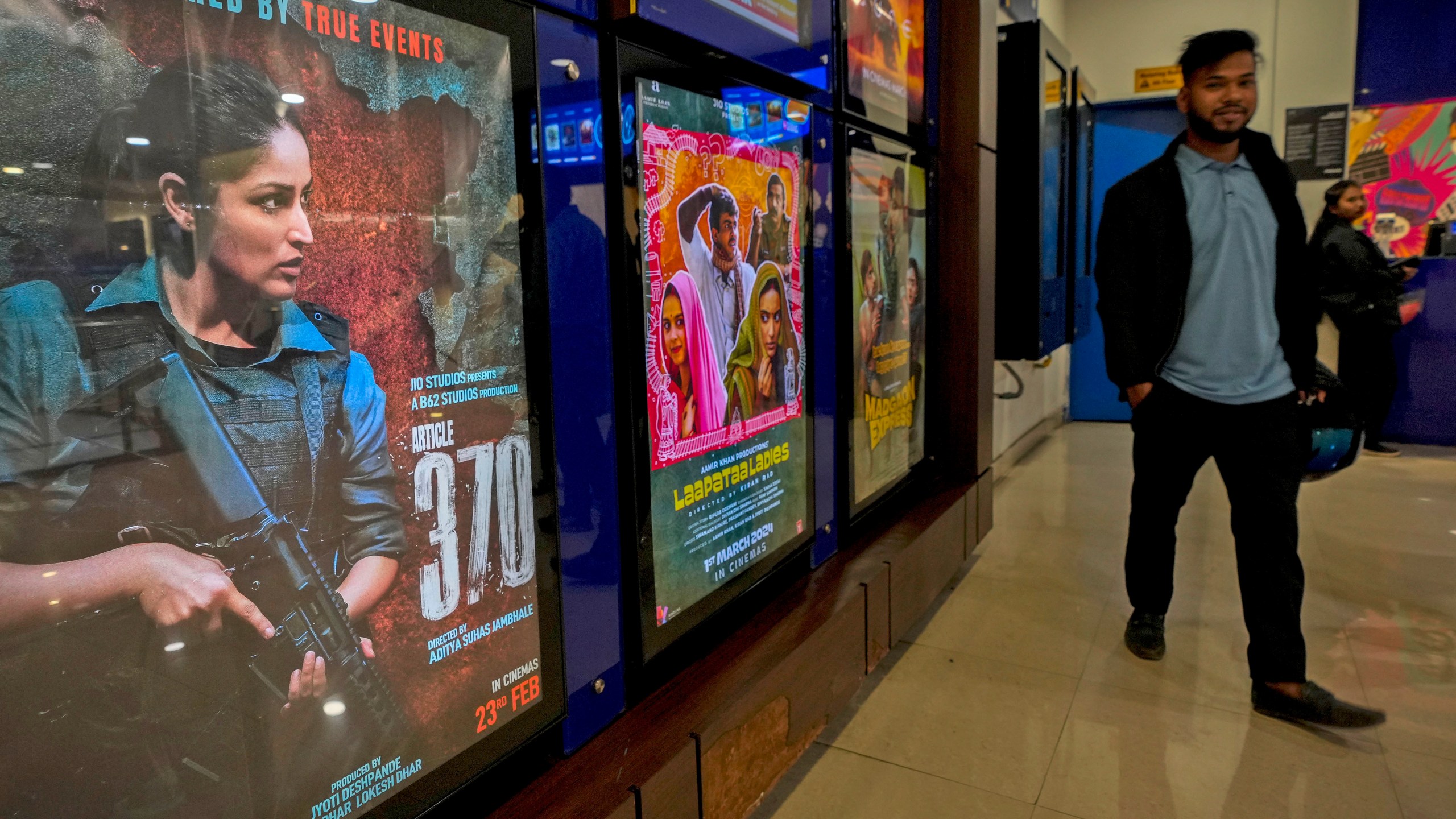 A man stands next to a poster of the movie Article 370 displayed at a cinema hall in Guwahati, India, Thursday, March 21, 2024. The movie is one of several upcoming Bollywood releases based on polarizing issues, which either promote Indian Prime Minister Narendra Modi and his government’s political agenda, or lambast his critics. (AP Photo/Anupam Nath)