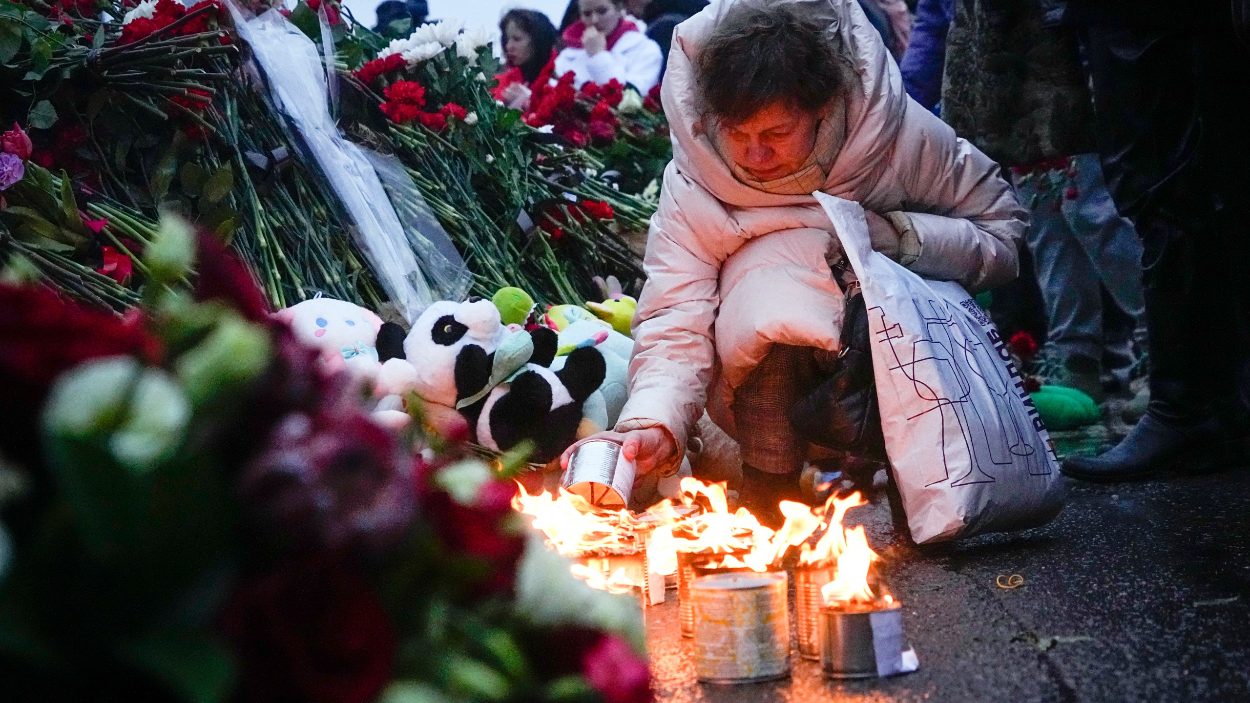 A woman lights candles at the fence next to the Crocus City Hall, on the western edge of Moscow, Russia, Saturday, March 23, 2024. Russia's top state investigative agency says the death toll in the Moscow concert hall attack has risen to over 133. The attack Friday on Crocus City Hall, a sprawling mall and concert venue on Moscow's western edge, also left many wounded and left the building a smoldering ruin. (AP Photo/Alexander Zemlianichenko)