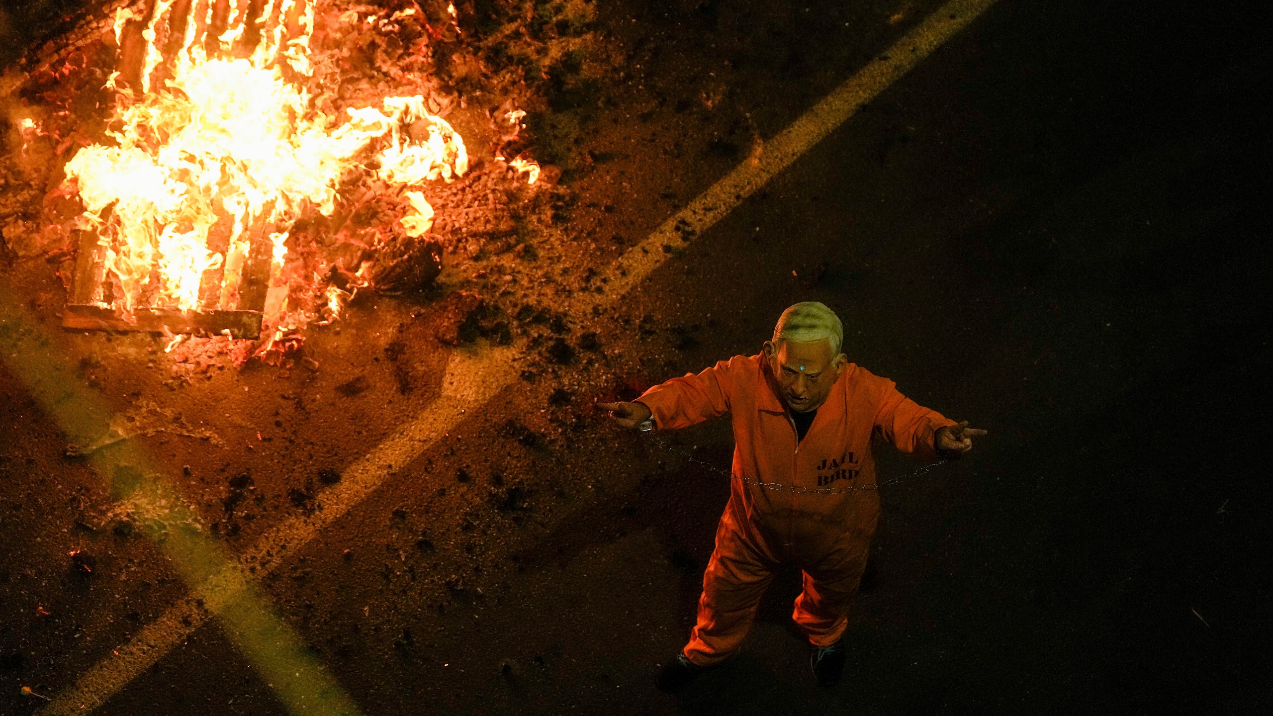 A demonstrator wearing a mask depicting Israeli Prime Minister Benjamin Netanyahu in a prisoner uniform blocks a road during a protest against Netanyahu's government and call for the release of hostages held in the Gaza Strip by the Hamas militant group, in Tel Aviv, Israel, Saturday, March 23, 2024. (AP Photo/Ariel Schalit)