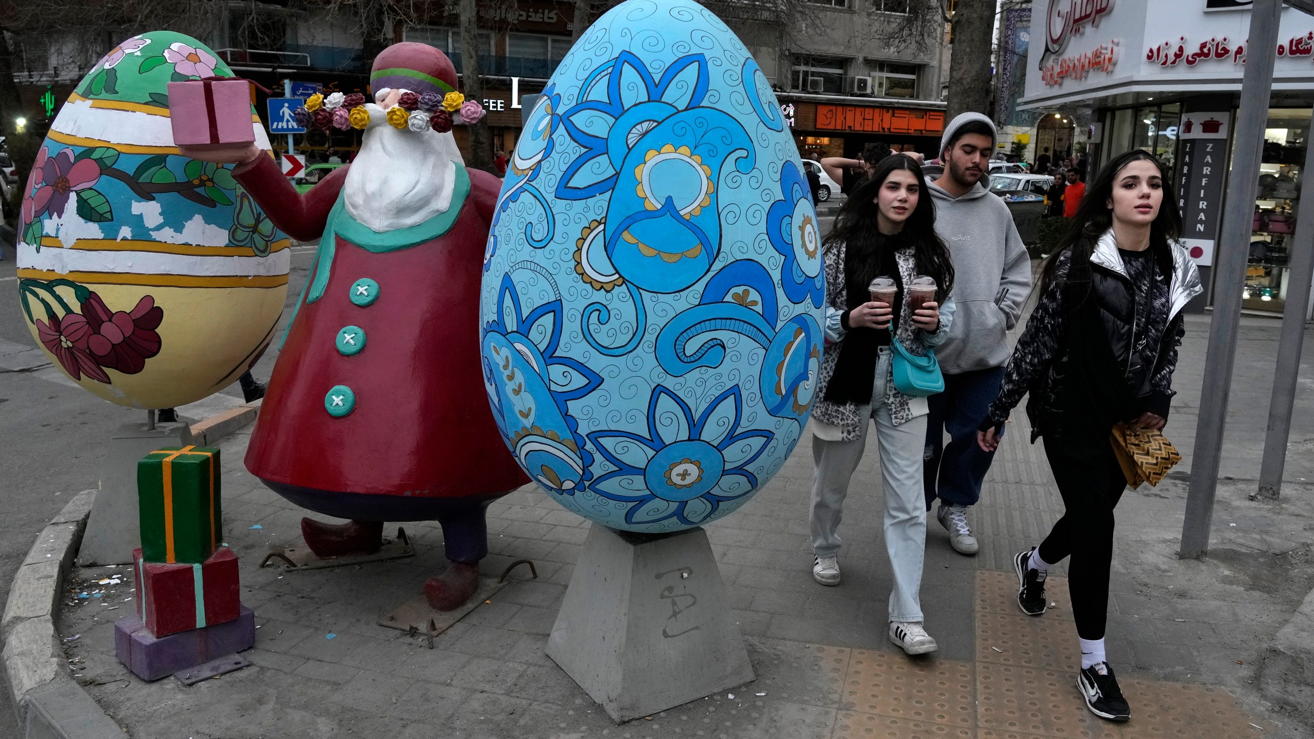 People walk past a statue of Amou Nowruz (Uncle Nowruz) and coloured eggs, symbols of the Iranian New Year, or Nowruz, in northern Tehran, Iran, Sunday, March 24, 2024. Iran's currency fell to a record low on Sunday, plunging to 613,500 to the dollar, as its people celebrated the Persian New Year. (AP Photo/Vahid Salemi)