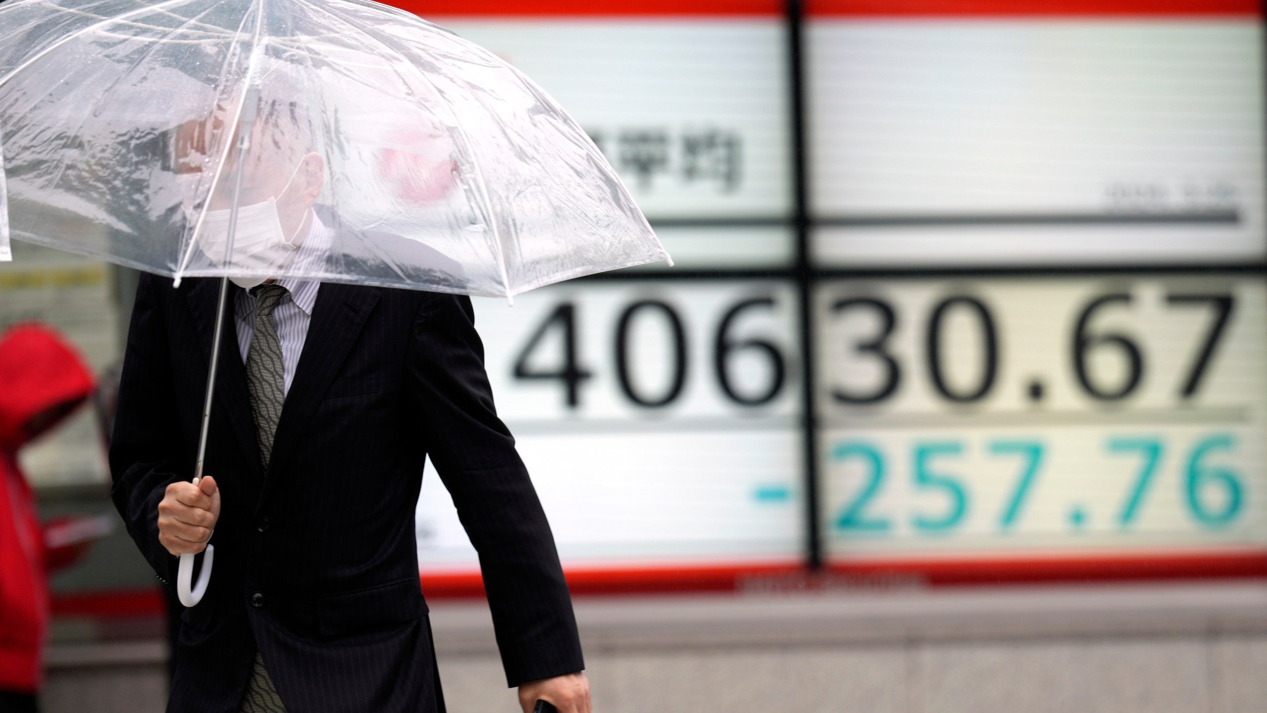 A person walks in front of an electronic stock board showing Japan's Nikkei 225 index at a securities firm in the rain Monday, March 25, 2024, in Tokyo. Asian shares were trading mixed on Monday, as investors awaited further indications the Federal Reserve might begin cutting interest rates.(AP Photo/Eugene Hoshiko)