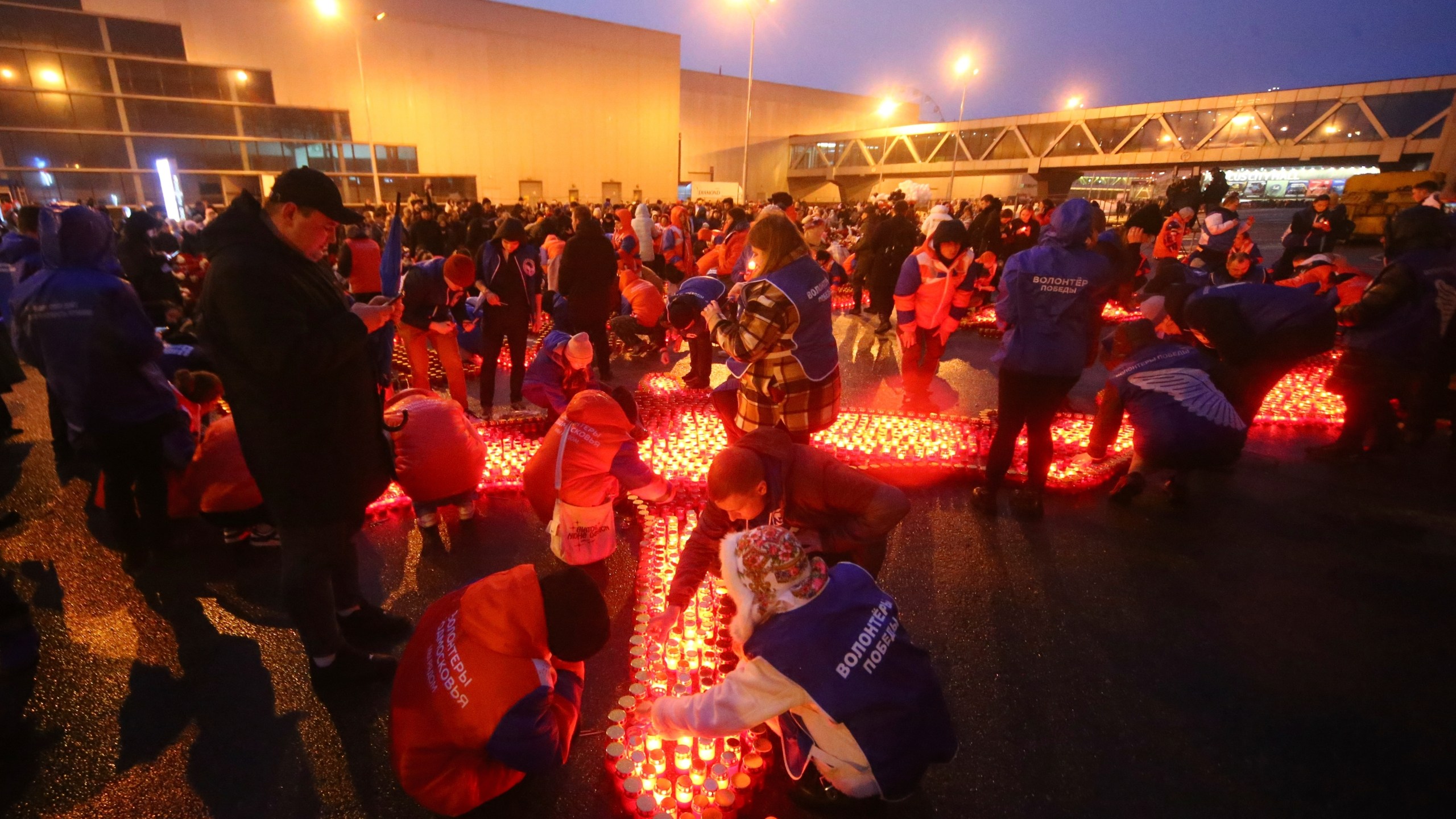 People light candles and lay flowers at a makeshift memorial in front of the Crocus City Hall on the western outskirts of Moscow, Russia, on Sunday, March 24, 2024. There were calls Monday for harsh punishment for those behind the attack on the Russia concert hall that killed more than 130 people as authorities combed the burnt-out ruins of the shopping and entertainment complex in search of more bodies. (Sergei Vedyashkin, Moscow News Agency via AP)