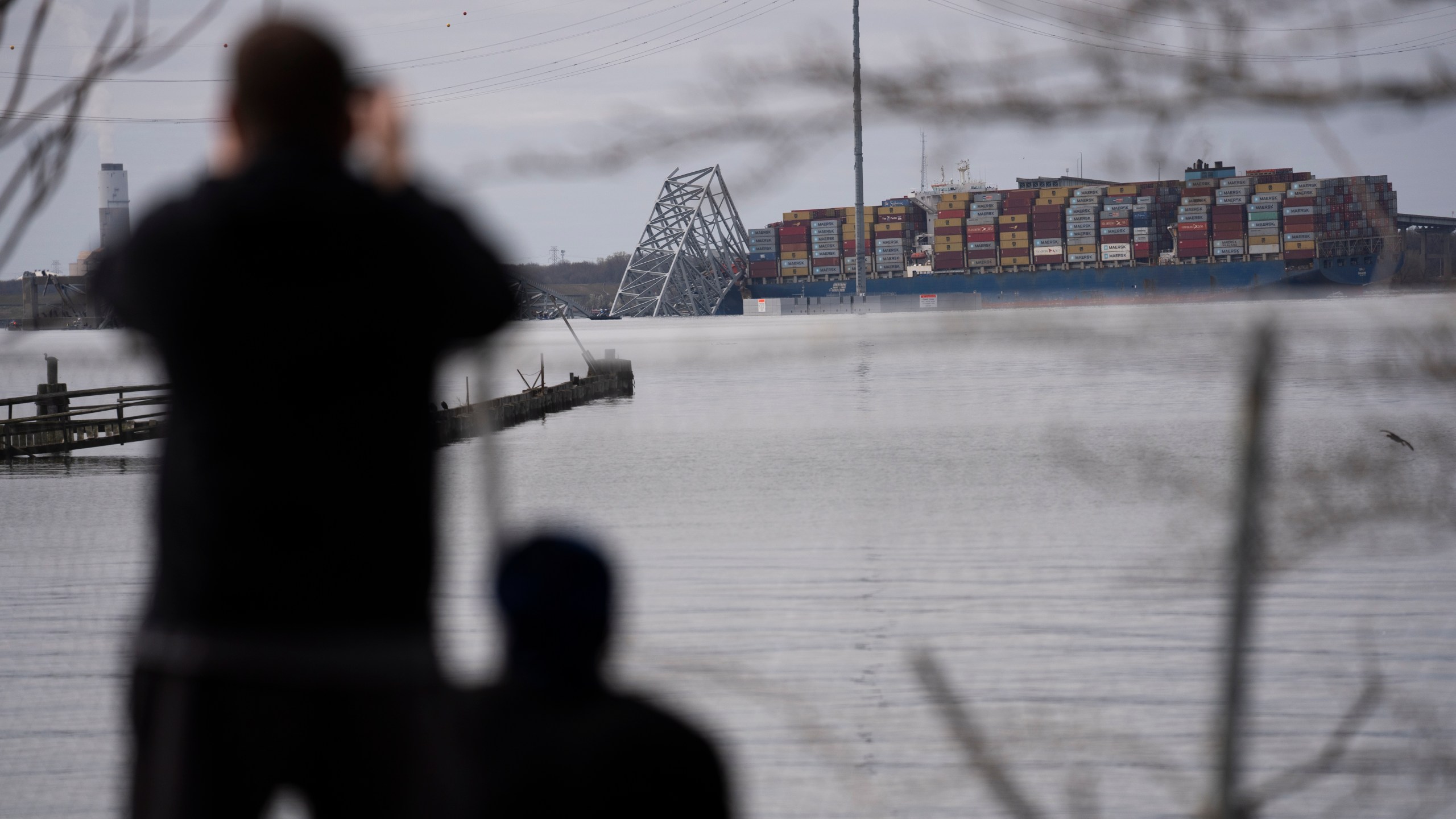 People view container ship as it rests against wreckage of the Francis Scott Key Bridge on Tuesday, March 26, 2024, as seen from Dundalk, Md. The ship rammed into the major bridge in Baltimore early Tuesday, causing it to collapse in a matter of seconds and creating a terrifying scene as several vehicles plunged into the chilly river below. (AP Photo/Matt Rourke)
