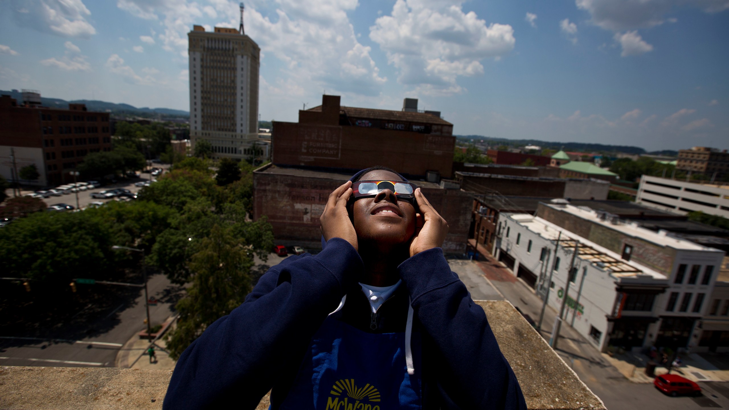FILE - Justin Coleman, of Birmingham, Ala., holds his glasses up to his eyes as he watches the solar eclipse atop a parking structure, Monday, Aug. 21, 2017, in Birmingham. Safe solar eclipse glasses block out the sun’s ultraviolet rays and nearly all visible light. When worn indoors, only very bright lights should be faintly visible – not household furniture or wallpaper. (AP Photo/Brynn Anderson, File)