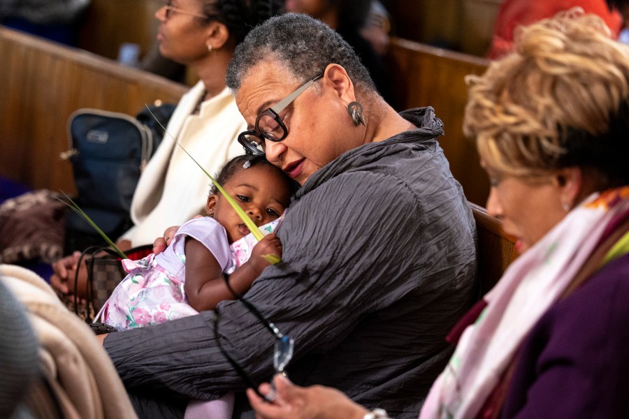 Marie Johns holds her her one-year-old daughter during Palm Sunday services at the Metropolitan AME Church in Washington, Sunday, March 24, 2024. Rev. William Lamar IV at Washington, D.C.’s historic Metropolitan AME has adjusted to offering both virtual and in-person services since the COVID-19 pandemic. After a noticeable attendance drop, more Metropolitan congregants are choosing in-person worship over virtual, even as they mourn members who died from COVID-19. (AP Photo/Amanda Andrade-Rhoades)