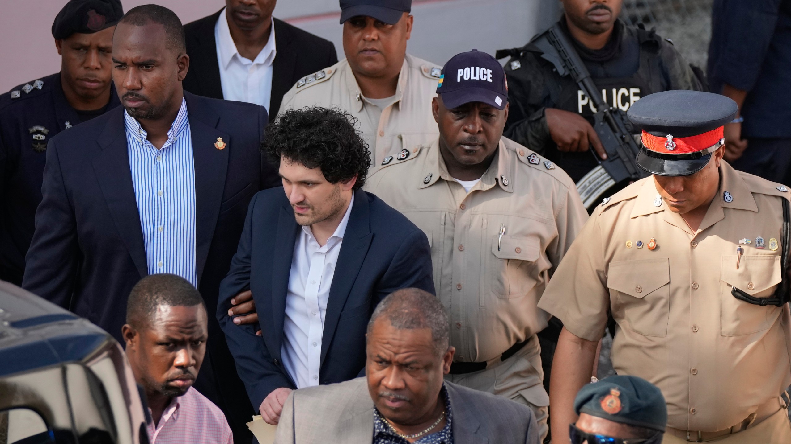 FILE - FTX founder Sam Bankman-Fried, center left, is escorted out of Magistrate Court following a hearing in Nassau, Bahamas, Dec. 19, 2022. Bankman-Fried, charged with a host of financial crimes, was arrested in the Bahamas on Dec. 12, 2022. (AP Photo/Rebecca Blackwell, File)