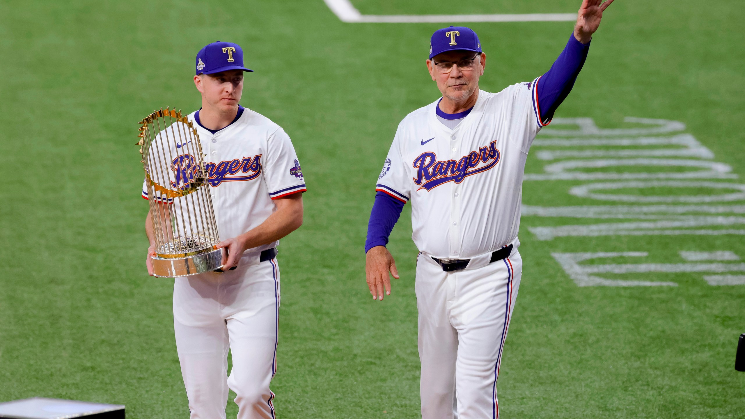 Texas Rangers relief pitcher Josh Sborz, left, and manager Bruce Bochy, right, walk the Commissioner's Trophy onto the field before the team's baseball game against the Chicago Cubs, Thursday, March 28, 2024 in Arlington, Texas. (AP Photo/Gareth Patterson)