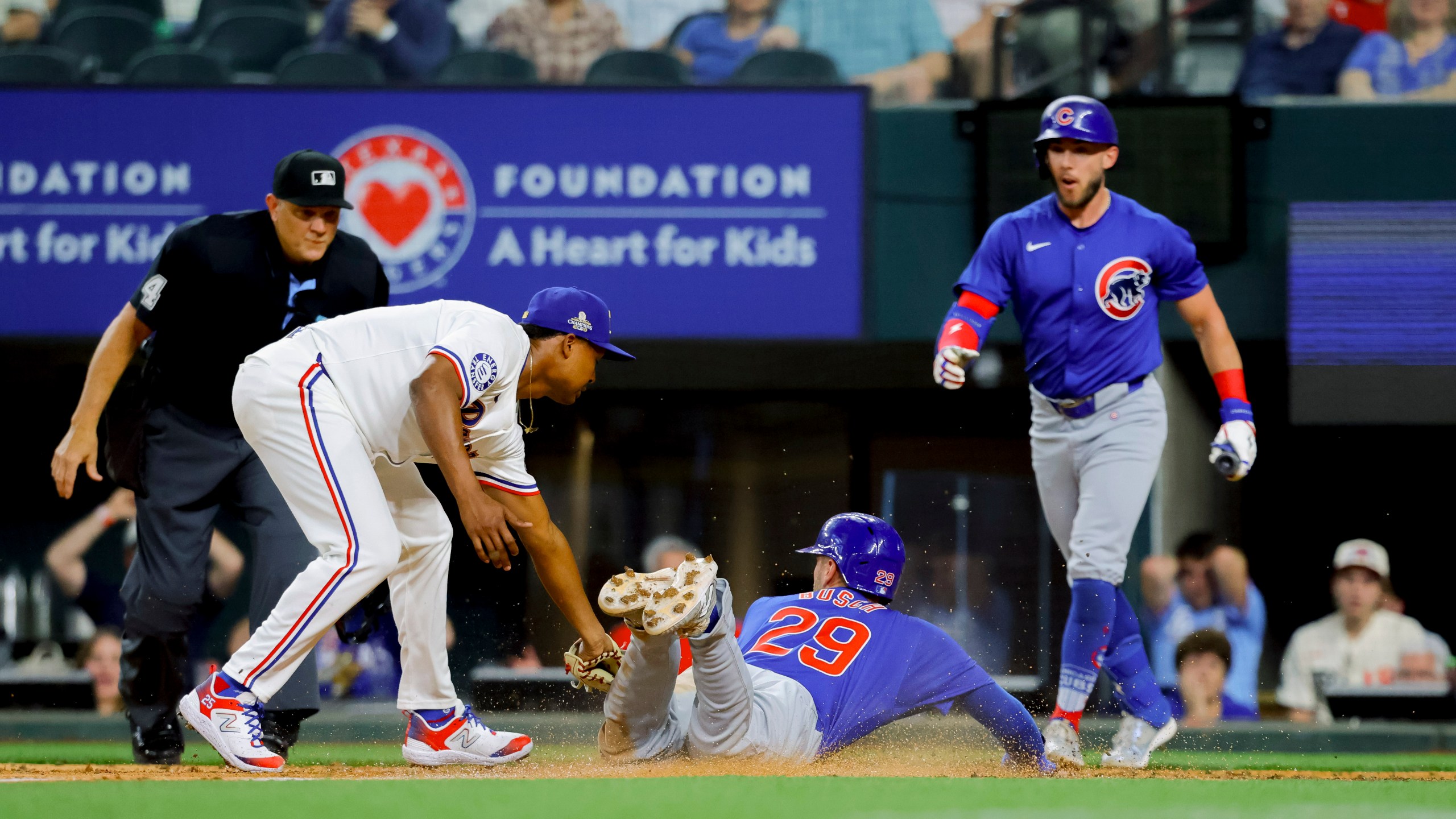 Chicago Cubs' Michael Busch (29) scores on a wild pitch as Texas Rangers pitcher José Leclerc, left, attempts the tag during the ninth inning of a baseball game Thursday, March 28, 2024 in Arlington, Texas. (AP Photo/Gareth Patterson)