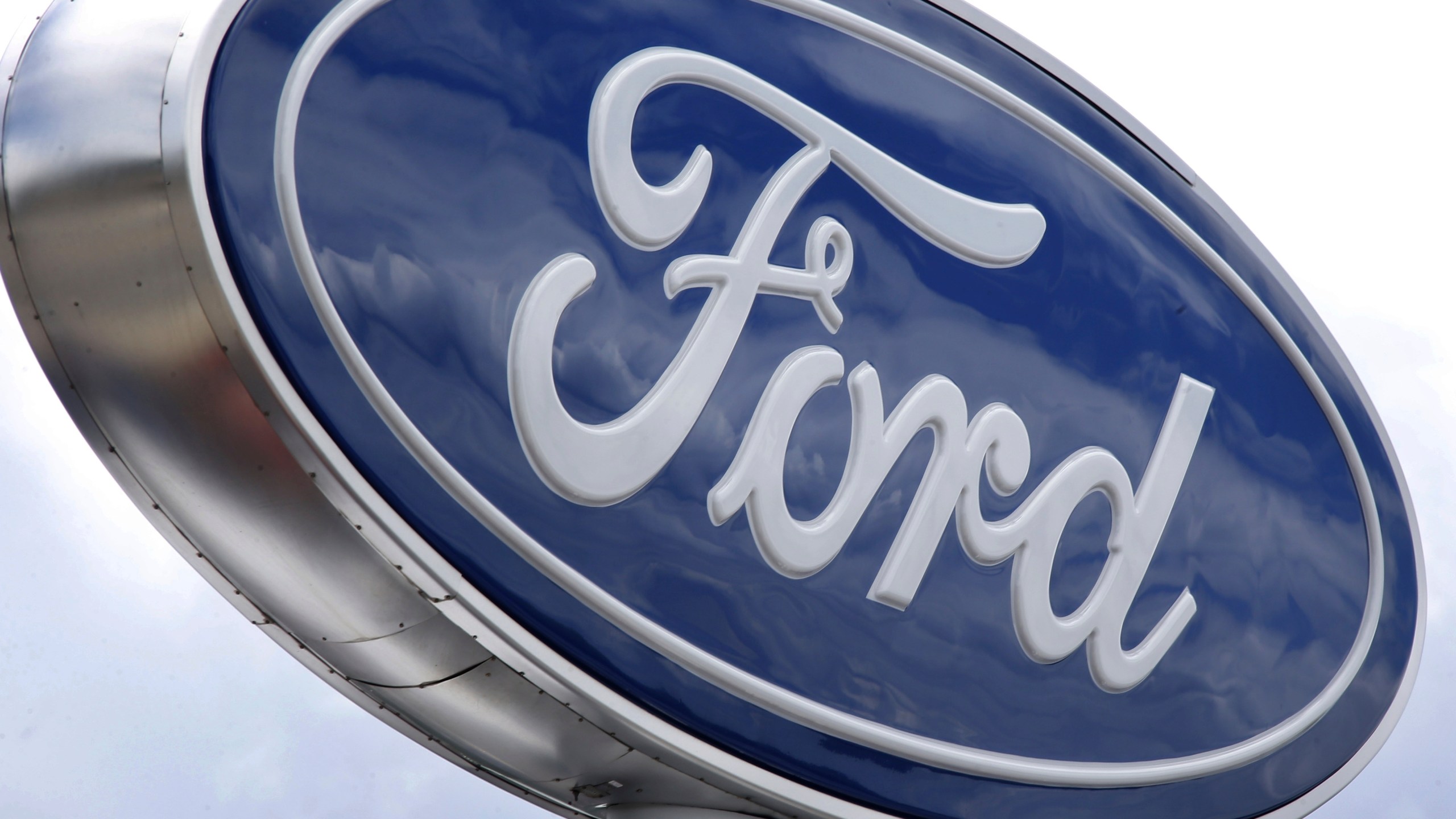 FILE - Clouds are reflected in the Ford sign at a dealership, June 5, 2014, in Wexford, Pa. U.S. auto safety regulators are investigating complaints that more than 540,000 Ford pickup trucks can abruptly downshift to a lower gear and increase the risk of a crash. (AP Photo/Keith Srakocic, File)